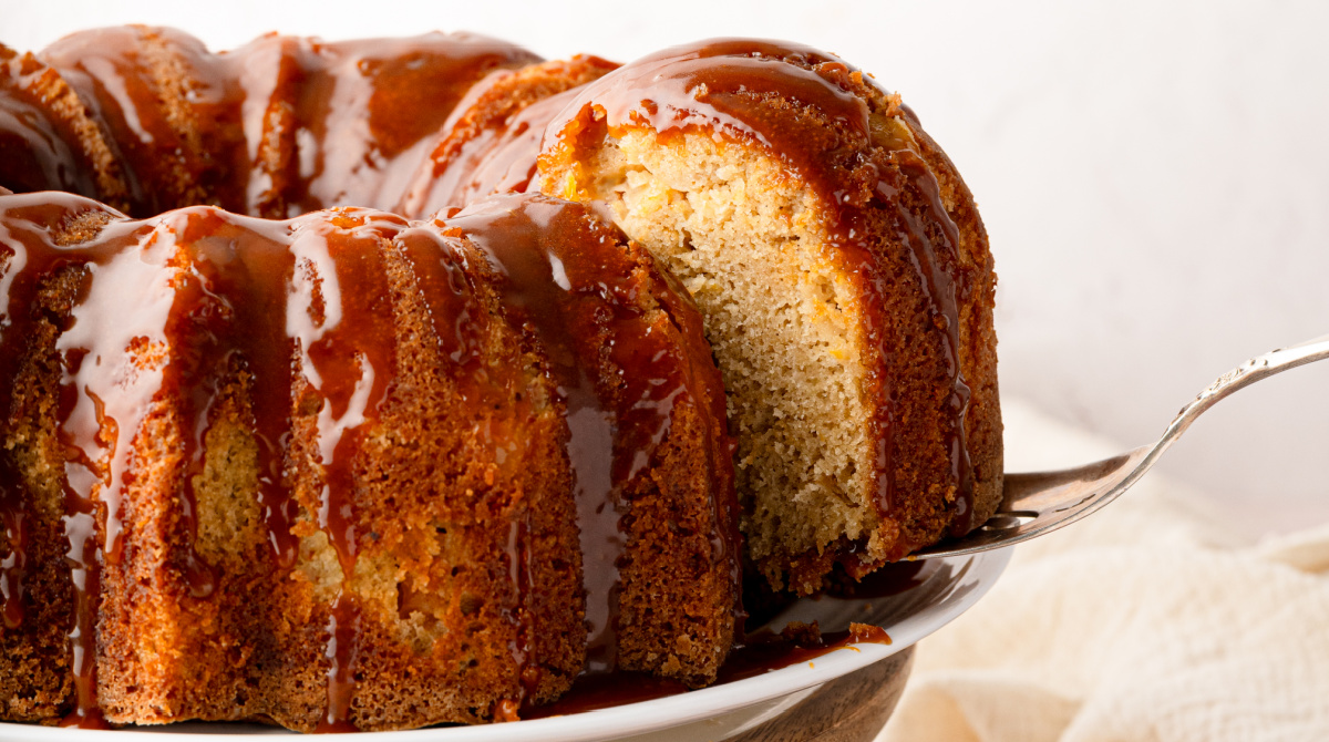 Peach cobbler Bundt cake with bourbon caramel showing peaches baked throughout the cake. Peach cobbler Bundt cake with bourbon caramel and a slice being lifted from the cake.