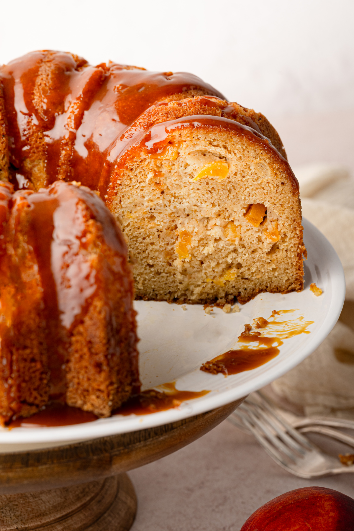 Cut peach cobbler Bundt cake showing peaches baked throughout the cake beneath the bourbon caramel. Interior of peach cobbler Bundt cake with bourbon caramel and peaches baked throughout.