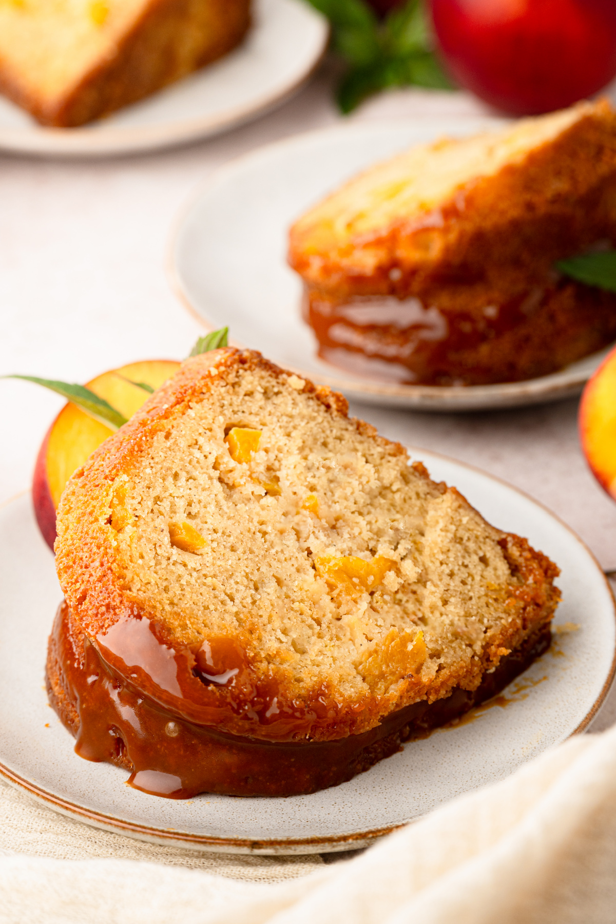 Peach cobbler Bundt cake slice topped with bourbon caramel and filled with pieces of peach. peach-cobbler-bundt-cake-slice-with-bourbon-caramel
