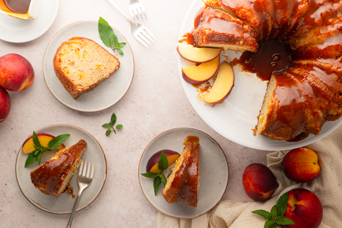 Peach cobbler Bundt cake drizzled with bourbon caramel and served with fresh peach slices. Overhead view of peach cobbler Bundt cake with bourbon caramel served with fresh peaches.