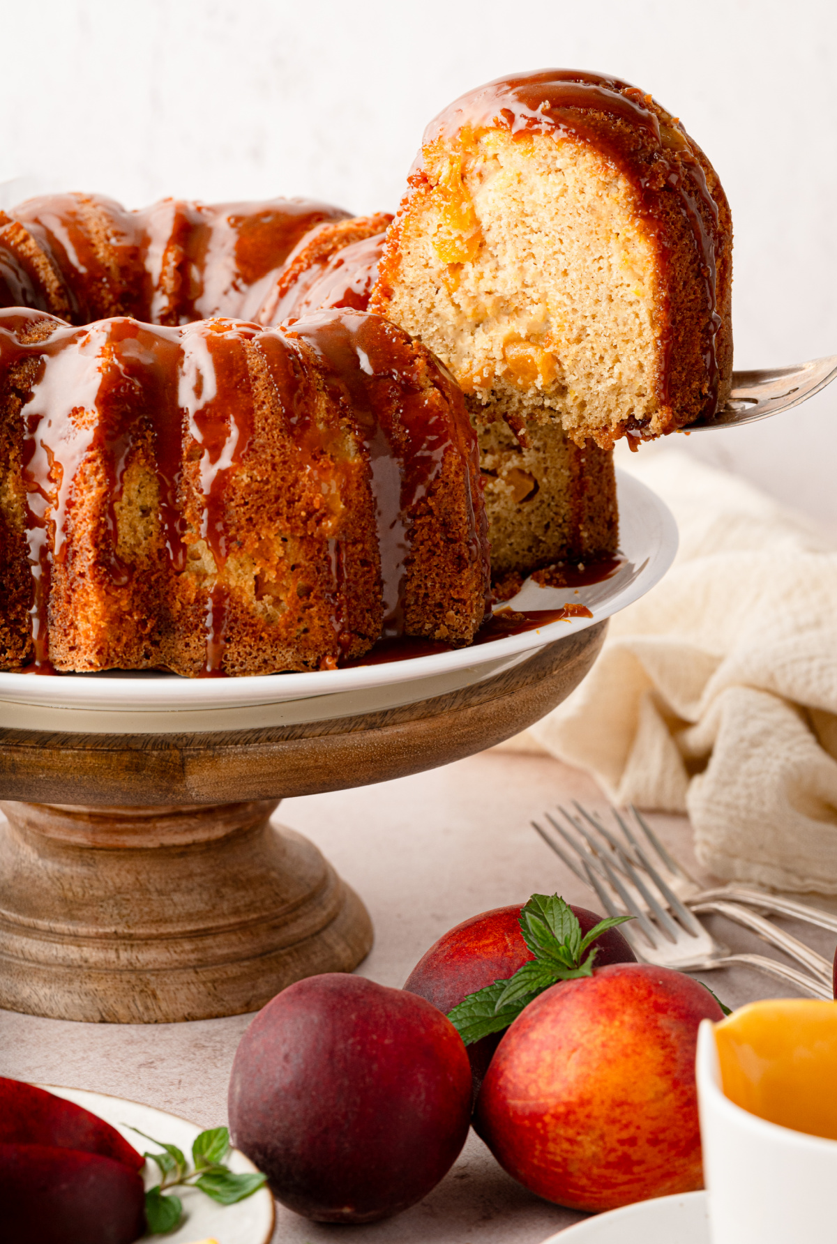 Peach cobbler Bundt cake with bourbon caramel and fresh peaches baked into every slice. Slice of peach cobbler Bundt cake with bourbon caramel showing peaches baked throughout the cake.