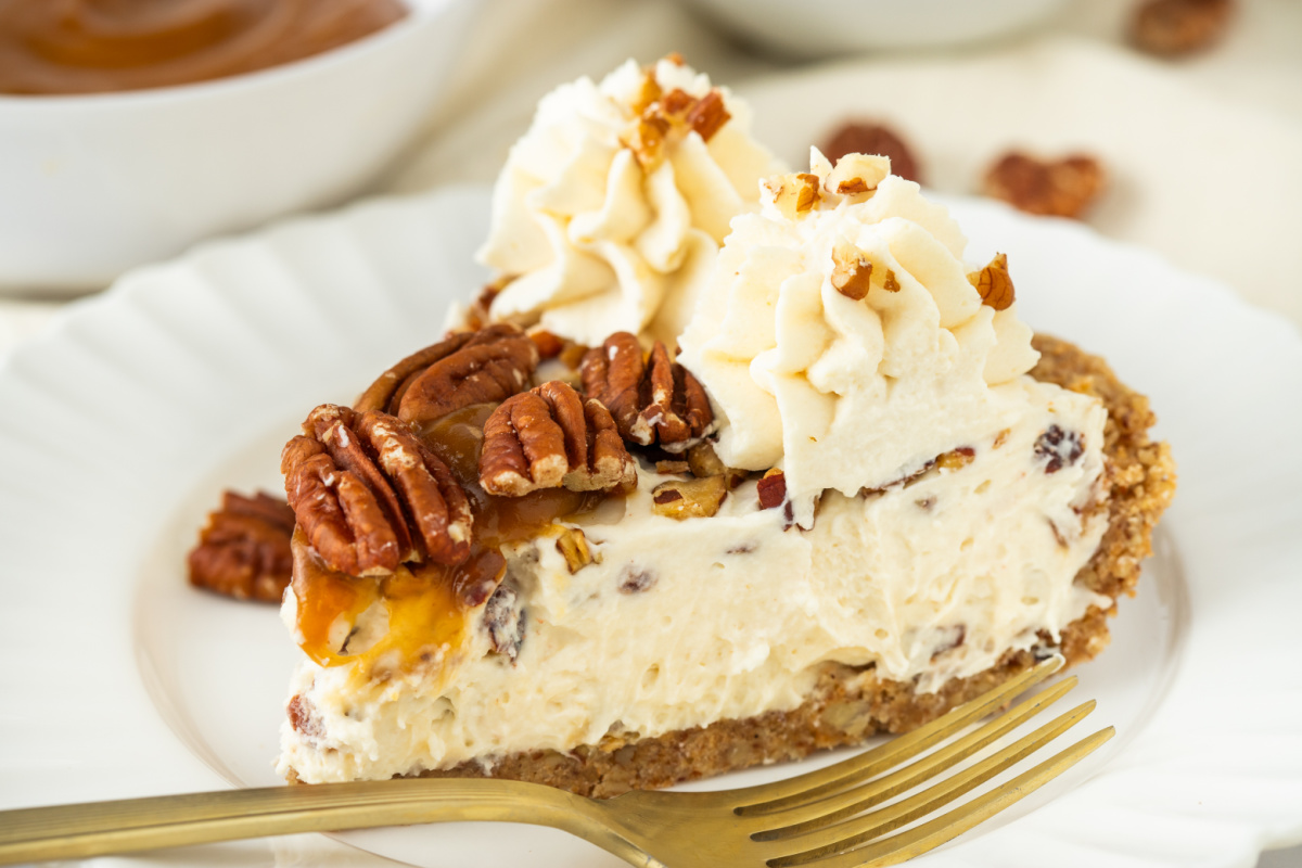 Easy Pecan Cream Pie Close-up slice of pecan cream pie with toasted pecans, whipped cream, caramel drizzle, and pecan crust
