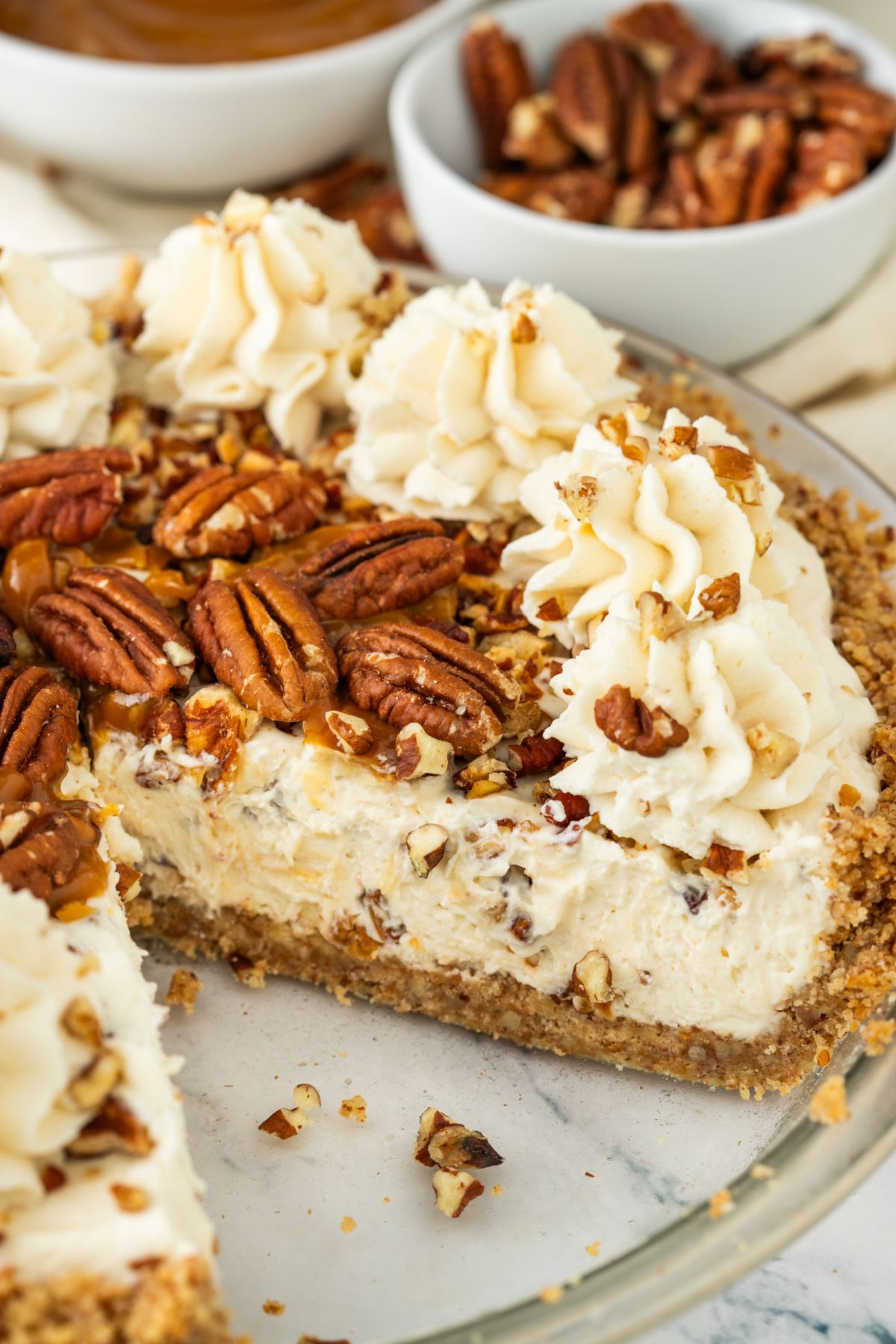 Pecan Dessert Recipe Pecan cream pie with a slice removed, showing the toasted pecan filling, pecan crust, whipped cream, and caramel topping