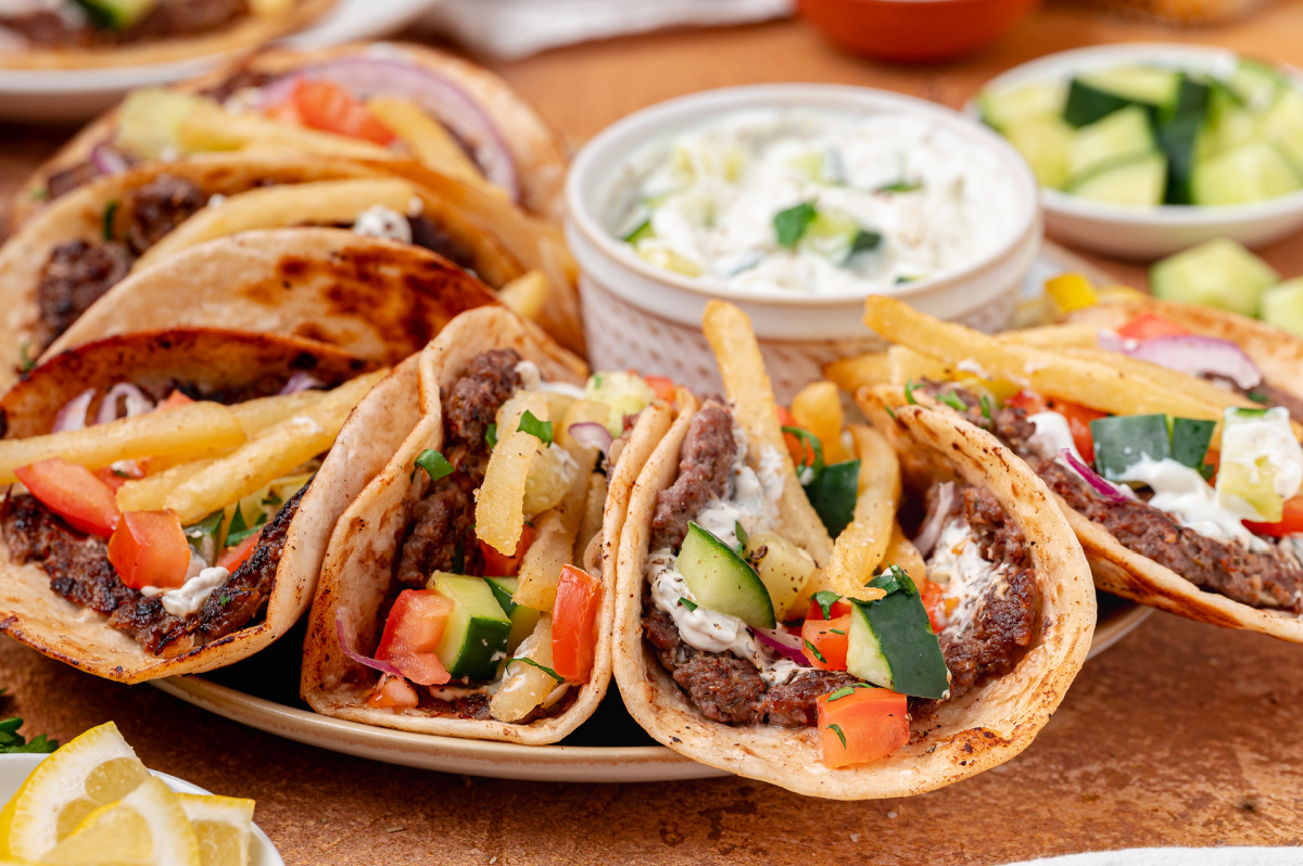 Smashed gyro tacos with crispy beef edges, cool tzatziki, and fries tucked inside. Smashed gyro tacos filled with seasoned beef, tzatziki, cucumber, tomato, red onion, and fries.
