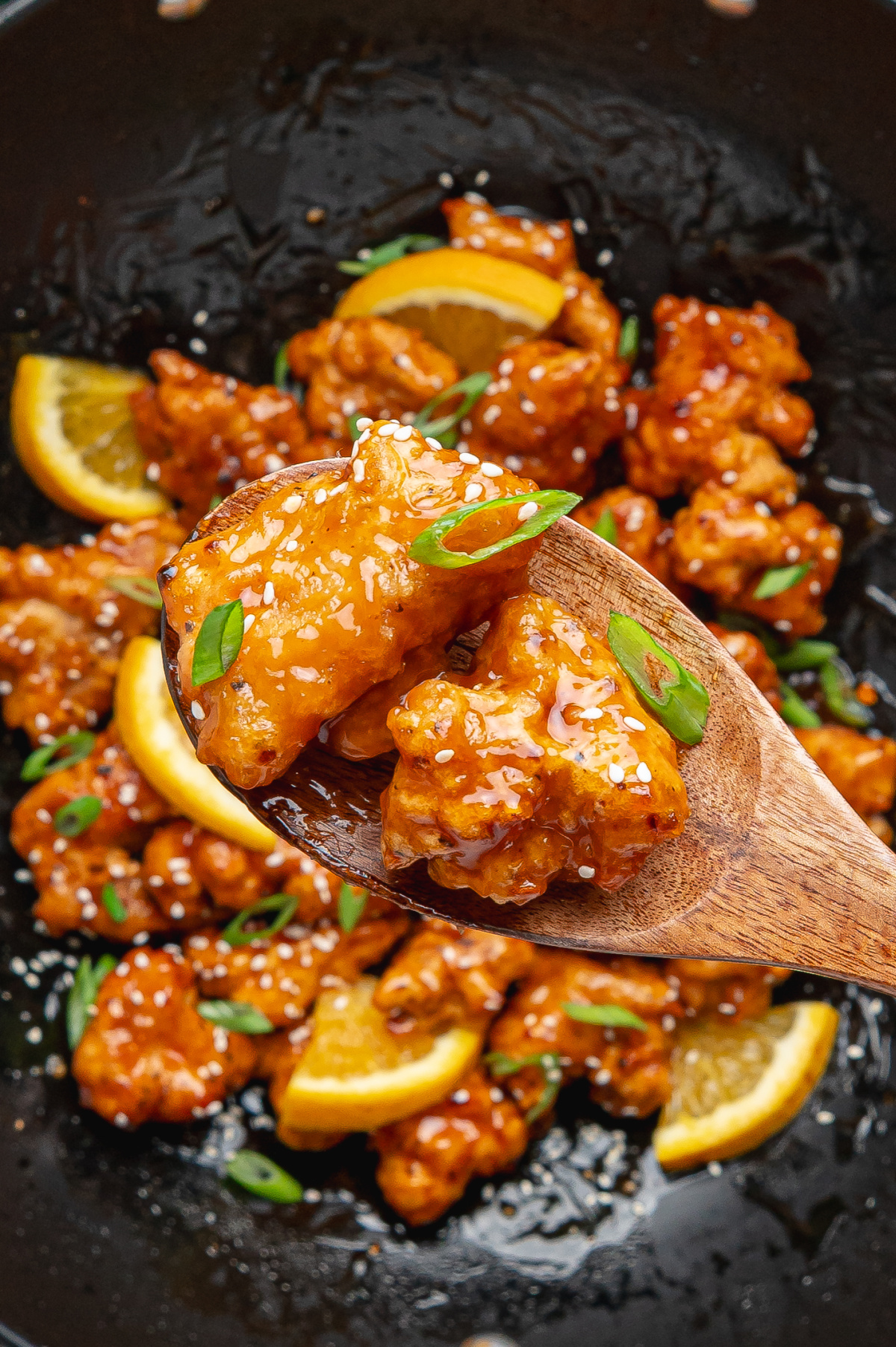 Orange chicken with crispy battered chicken coated in homemade orange sauce on a wooden spoon above a wok.