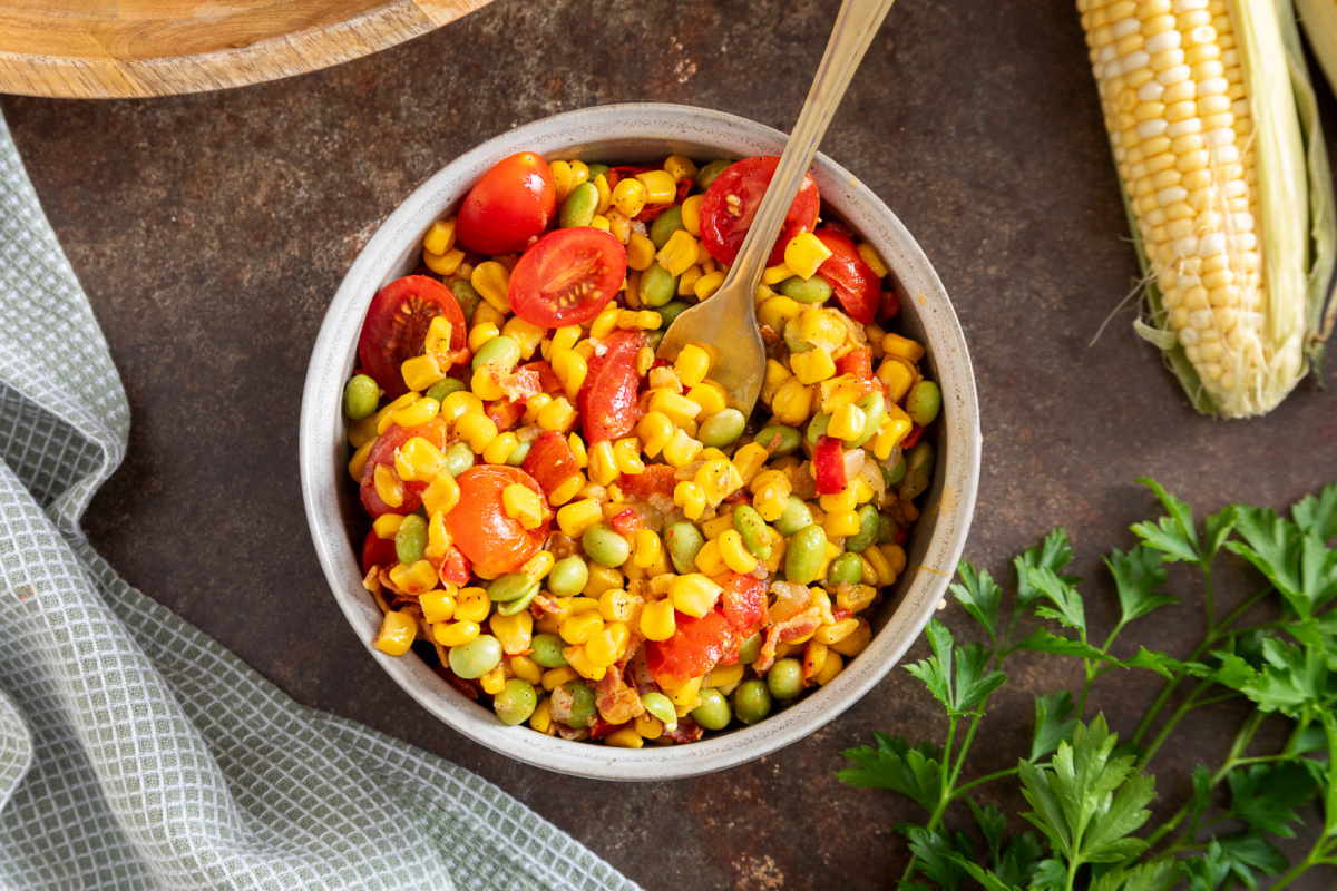 Overhead view of succotash with edamame, sweet corn, tomatoes, and bacon in a serving bowl