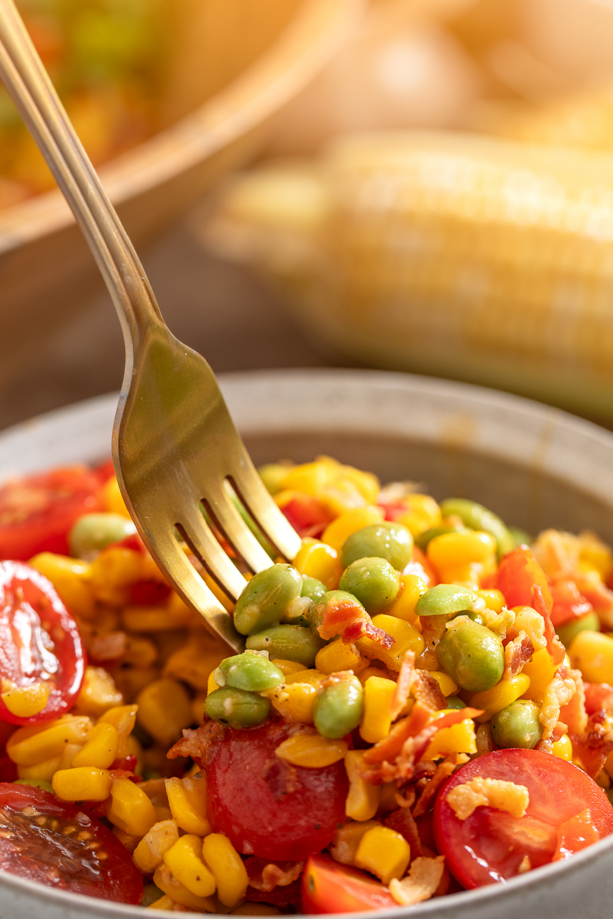 Fork lifting sweet corn, edamame, bacon, and tomatoes from a summer vegetable side dish