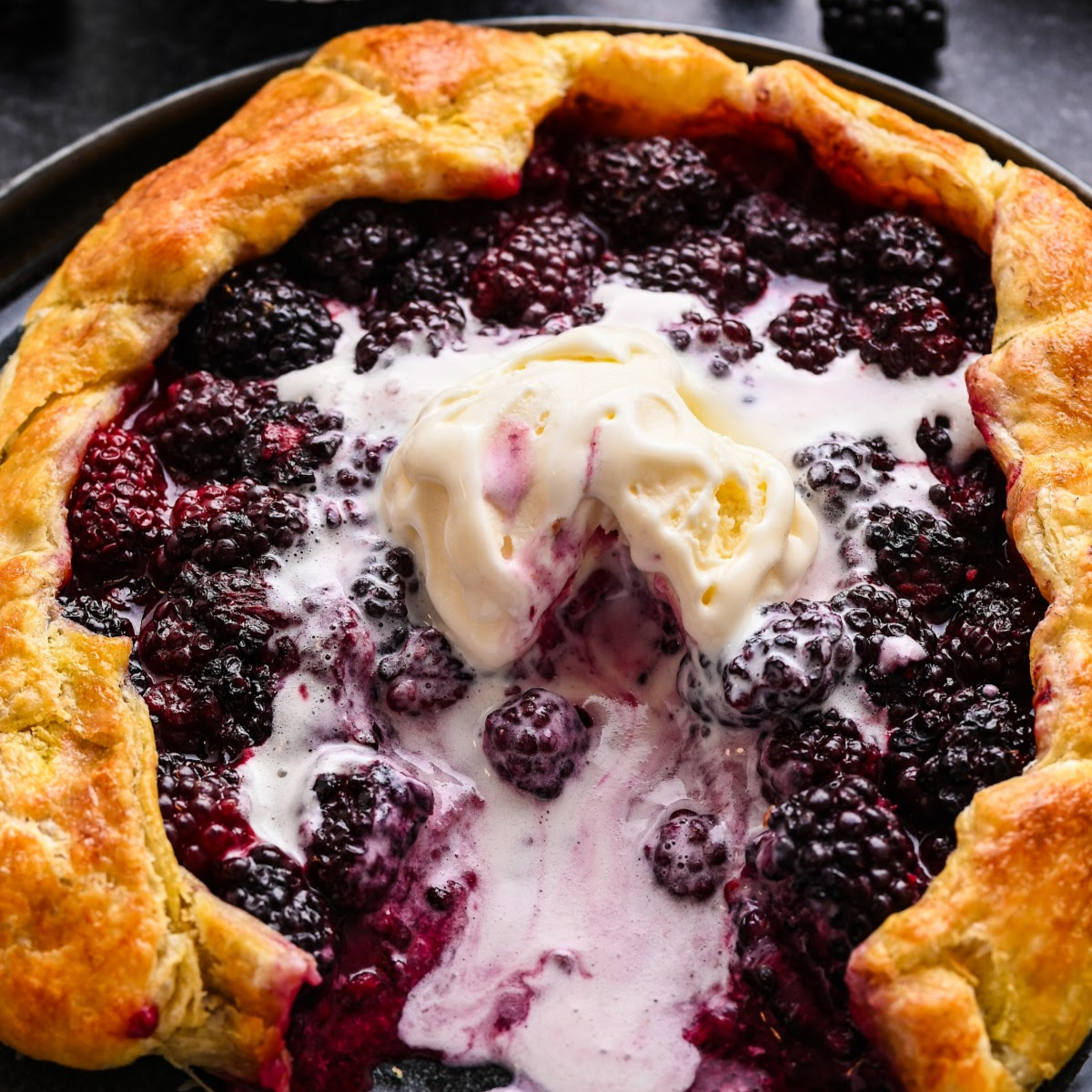 Overhead view of a blackberry puff pastry galette baked until golden and served with vanilla ice cream.