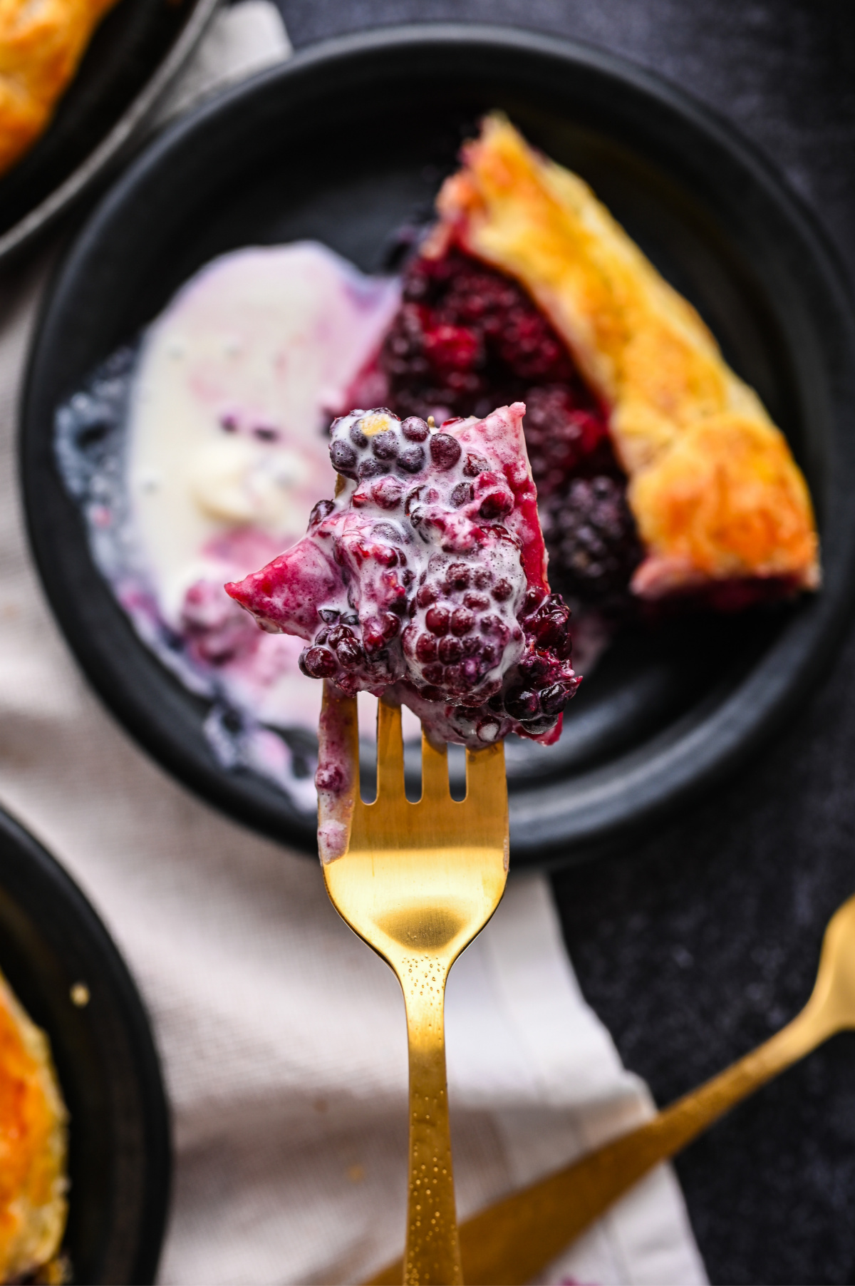 One bite of Blackberry Puff Pastry Galette with fresh blackberries and vanilla ice cream. Fork holding a bite of blackberry puff pastry galette with melting vanilla ice cream.