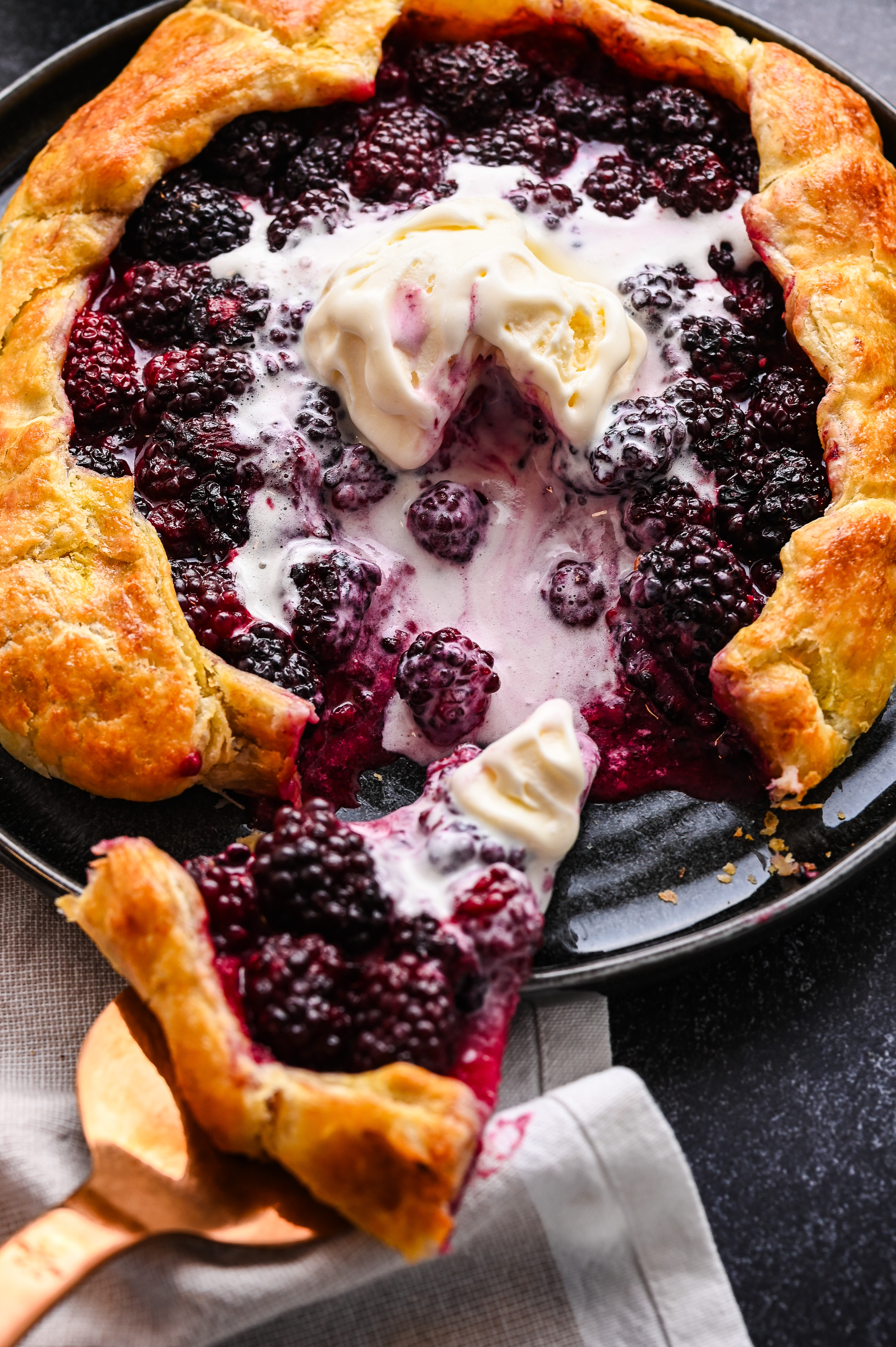 Serving Blackberry Puff Pastry Galette warm with vanilla ice cream. Serving a slice of blackberry puff pastry galette with vanilla ice cream.