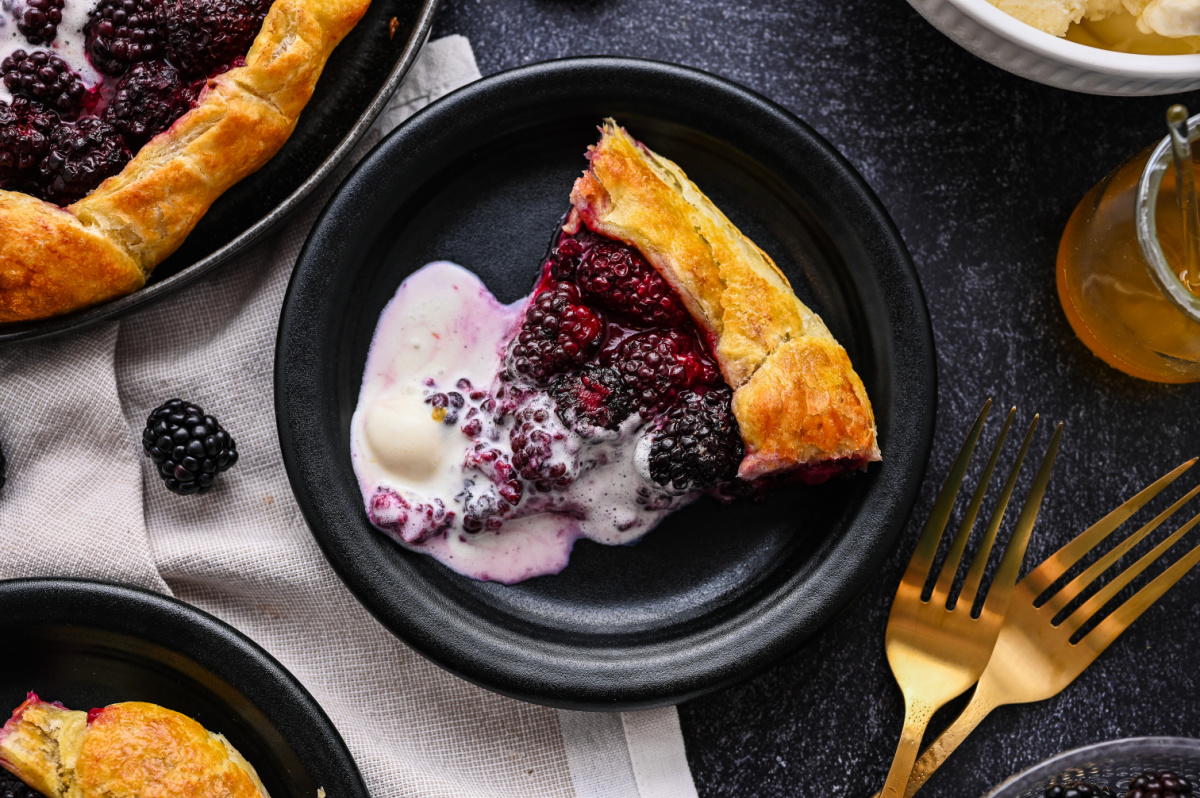 A slice of Blackberry Puff Pastry Galette served warm with vanilla ice cream. Slice of blackberry puff pastry galette served with melting vanilla ice cream.