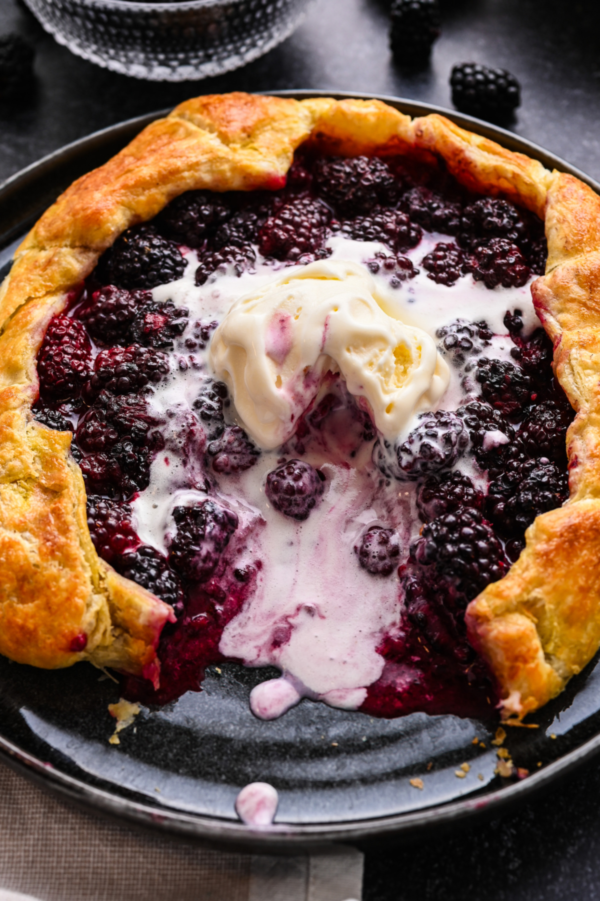 Blackberry Puff Pastry Galette with fresh blackberries and vanilla ice cream. Blackberry puff pastry galette topped with vanilla ice cream on a black plate.