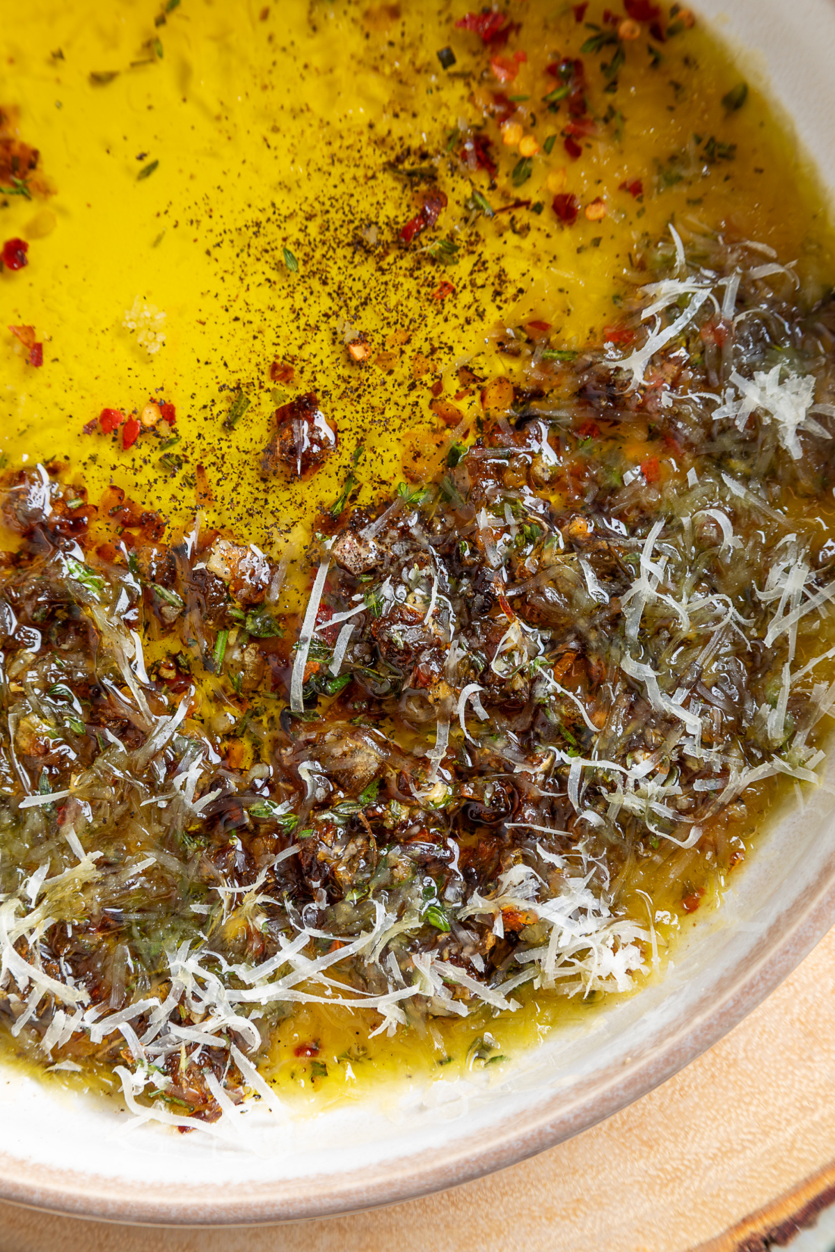Bread Dipping Oil detail Close-up of bread dipping oil with caramelized shallots, Parmesan, fresh herbs, and cracked black pepper.