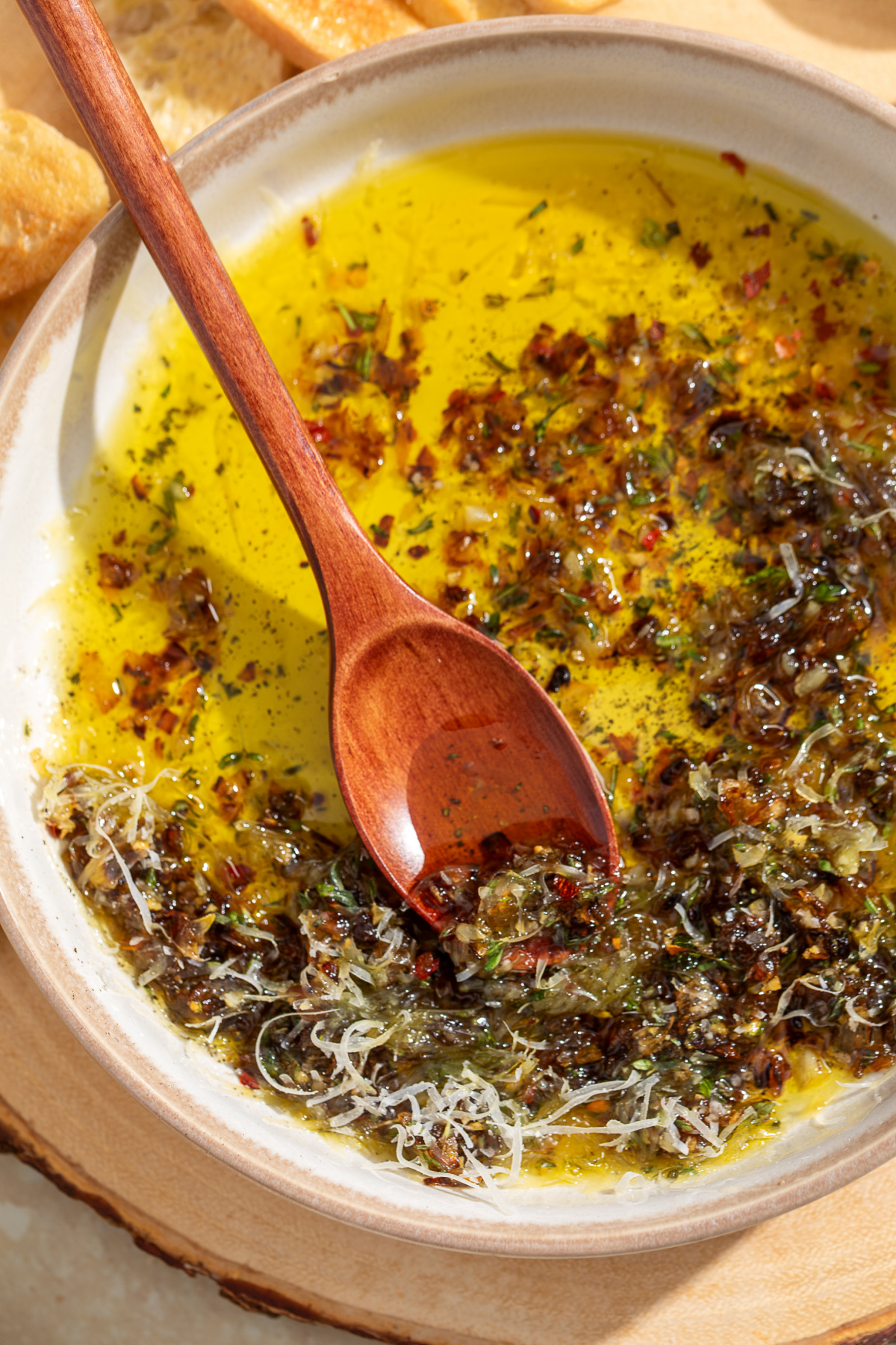 Serving Bread Dipping Oil Wooden spoon scooping caramelized shallots from bread dipping oil with Parmesan, fresh herbs, and olive oil.