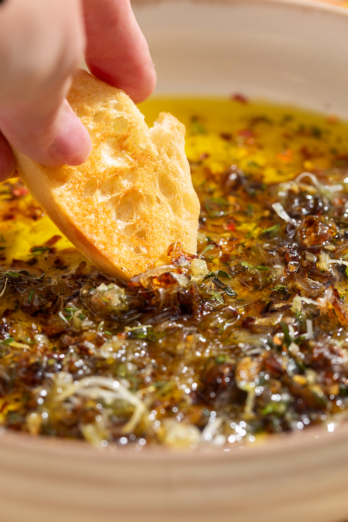 Dipping Bread into Bread Dipping Oil Toasted bread dipping into bread dipping oil with caramelized shallots, fresh herbs, and Parmesan.
