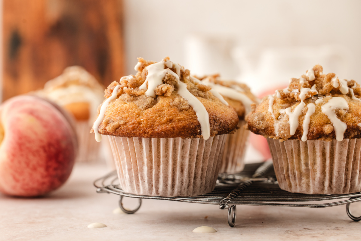 Brown butter peach coffee cake muffins cooling on a wire rack with fresh peaches
