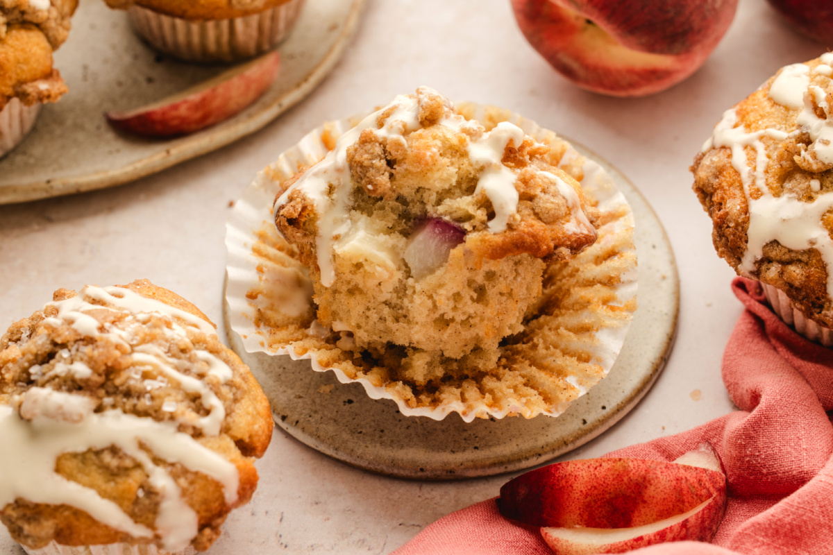 Inside of a brown butter peach coffee cake muffin showing fresh peach pieces, cinnamon streusel, and vanilla glaze