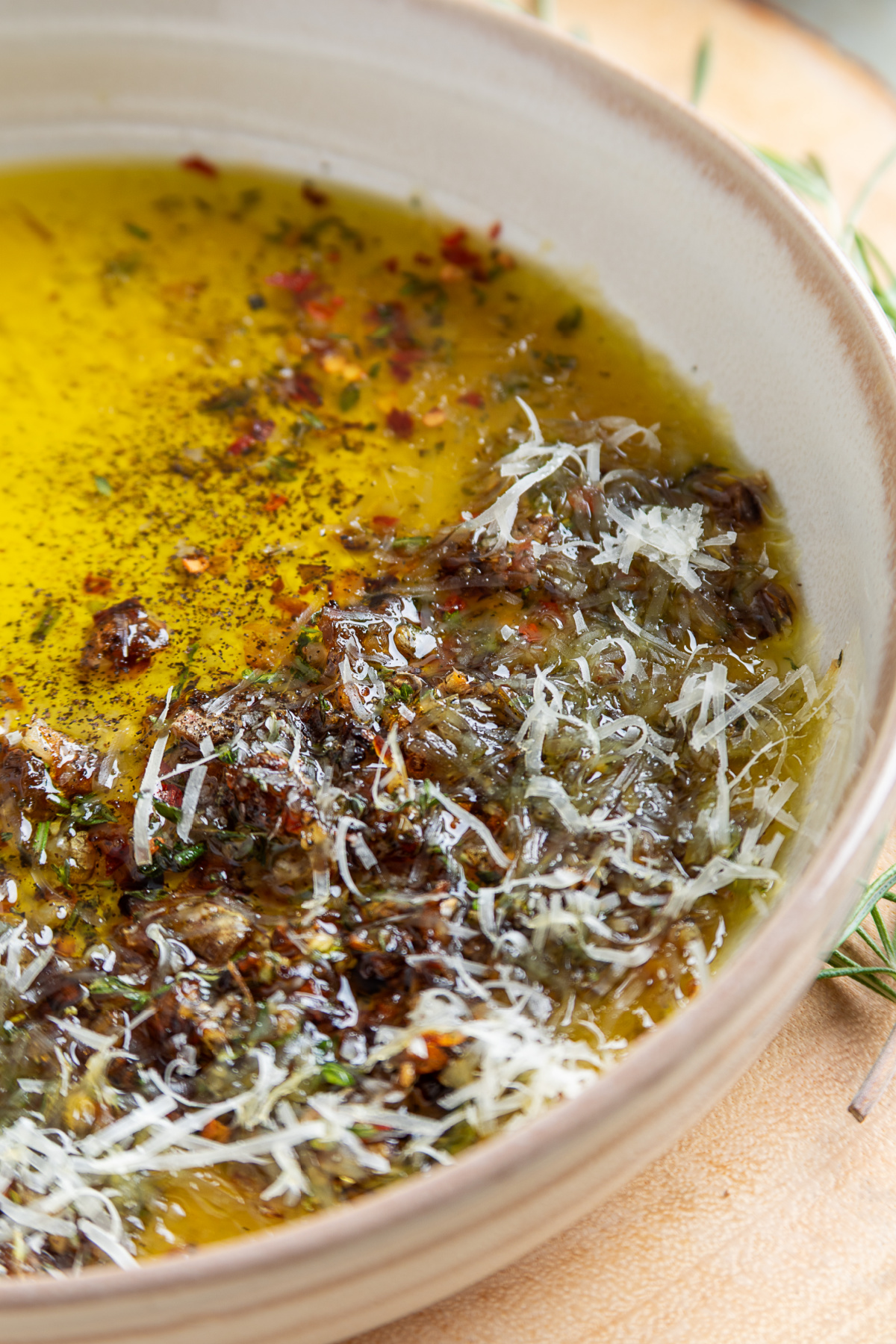 Close-up of caramelized shallot bread dipping oil with Parmesan, fresh herbs, cracked black pepper, and toasted baguette slices.