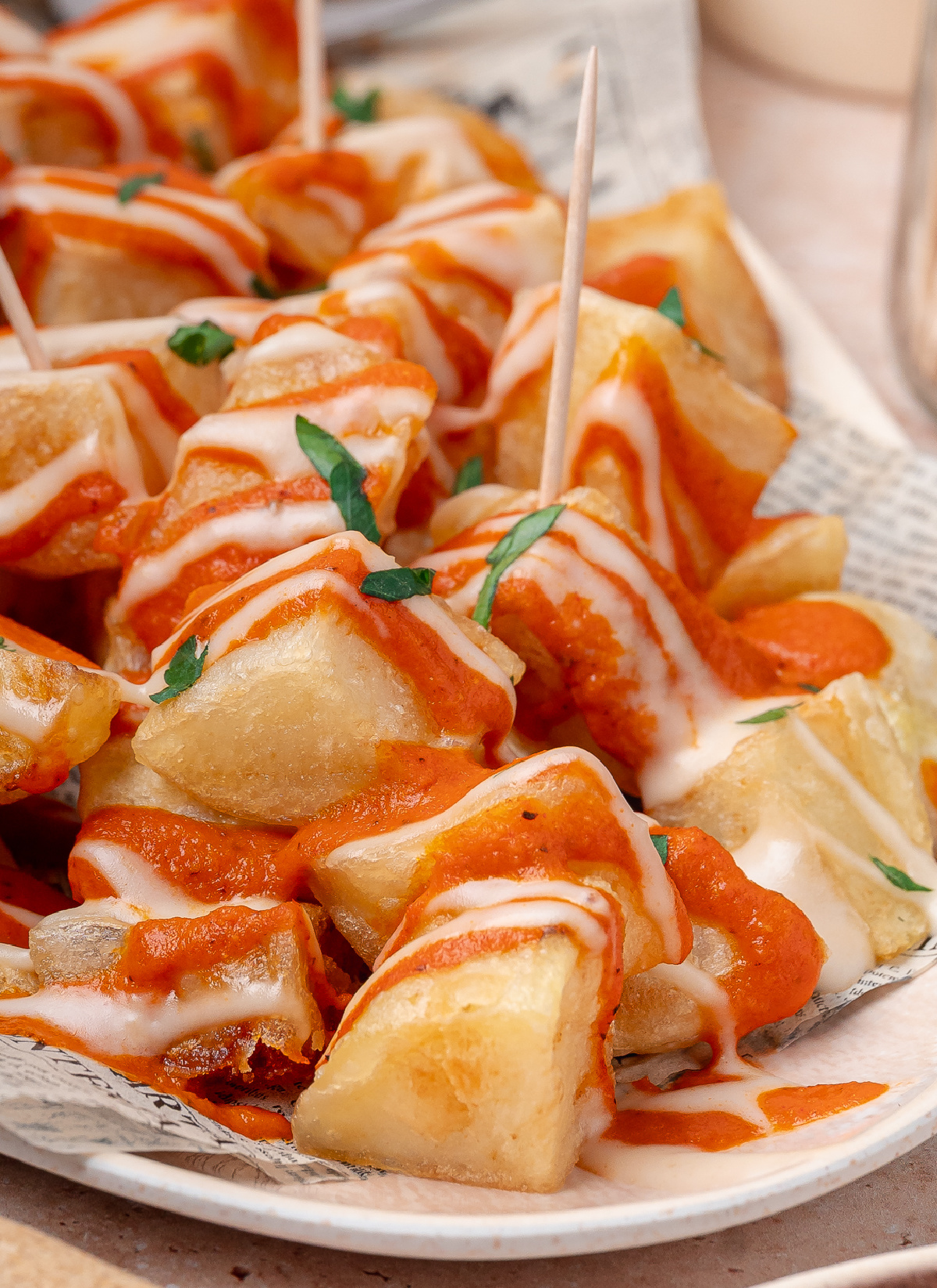 Crispy Bravas Potatoes Close-up of crispy fried potatoes topped with homemade bravas sauce, garlic aioli, and fresh parsley.