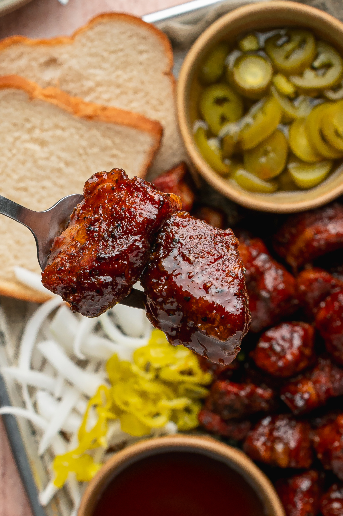 Fork holding two Peach Tea Pork Belly Burnt Ends coated in a glossy caramelized peach tea glaze.