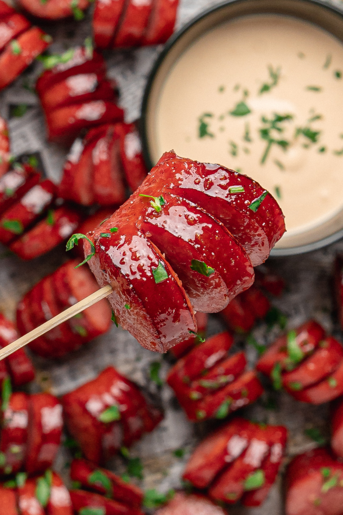 A honey garlic kielbasa bite showing the hasselback cuts filled with glossy glaze. Close-up of a glazed honey garlic kielbasa bite on a skewer with creamy honey mustard.