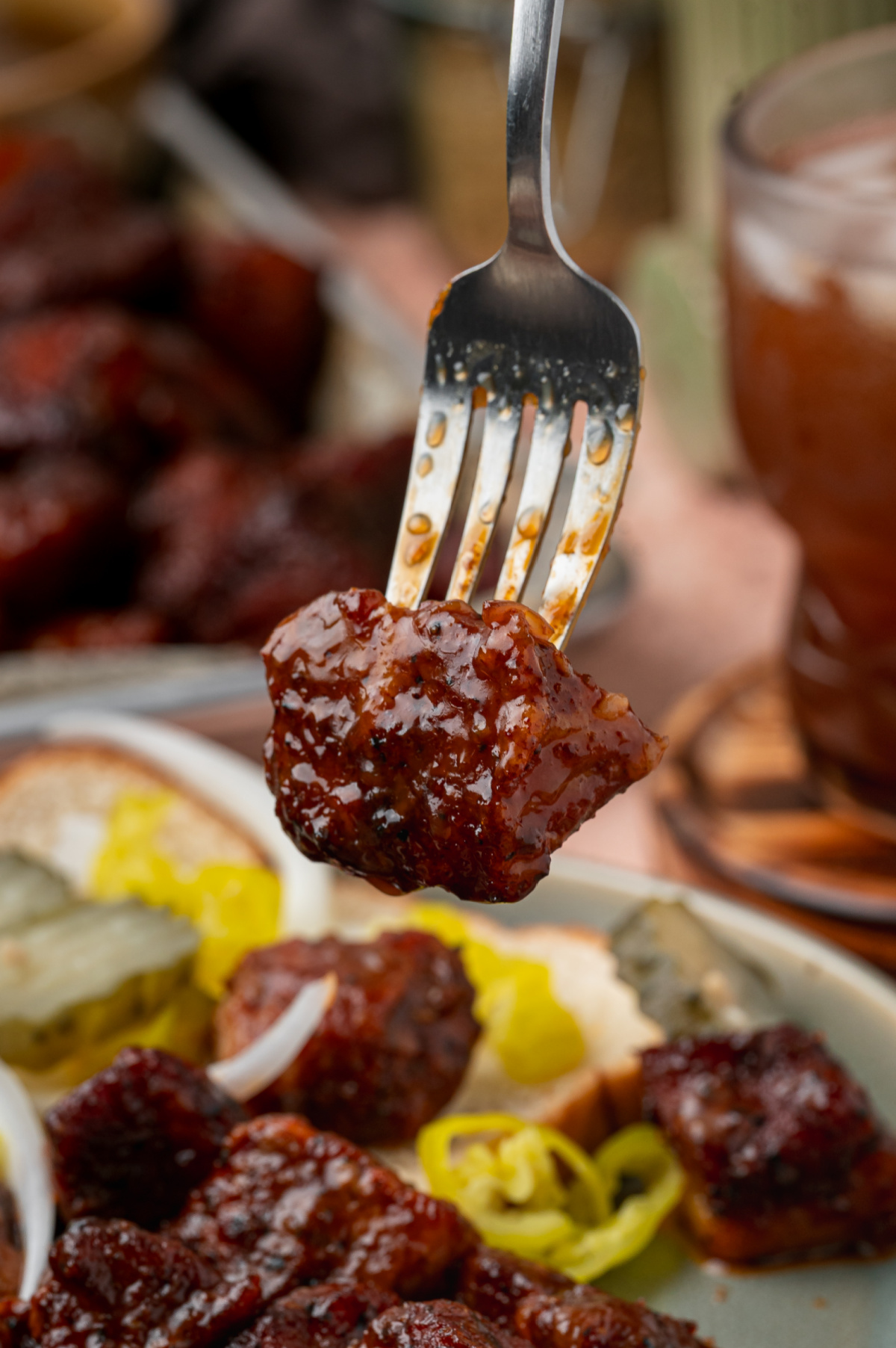 Close-up of a caramelized pork belly burnt end coated in glossy peach tea glaze on a fork.