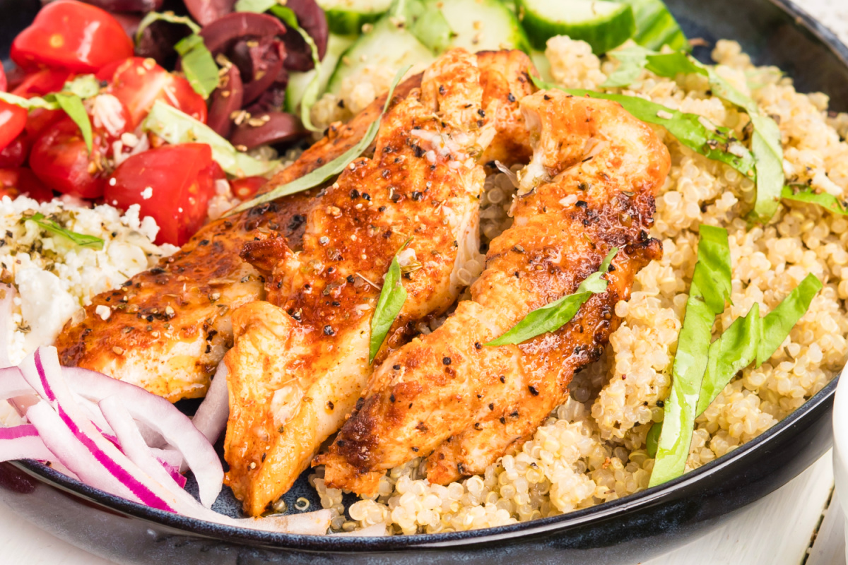 Close-up of Mediterranean Chicken Bowl Mediterranean chicken bowl with grilled chicken, quinoa, cherry tomatoes, cucumber, feta, Kalamata olives, fresh basil, and lemon vinaigrette.