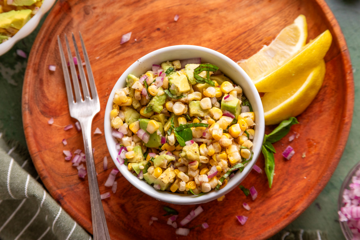 Individual serving of grilled corn salad with avocado, basil, and red onion in a small bowl.