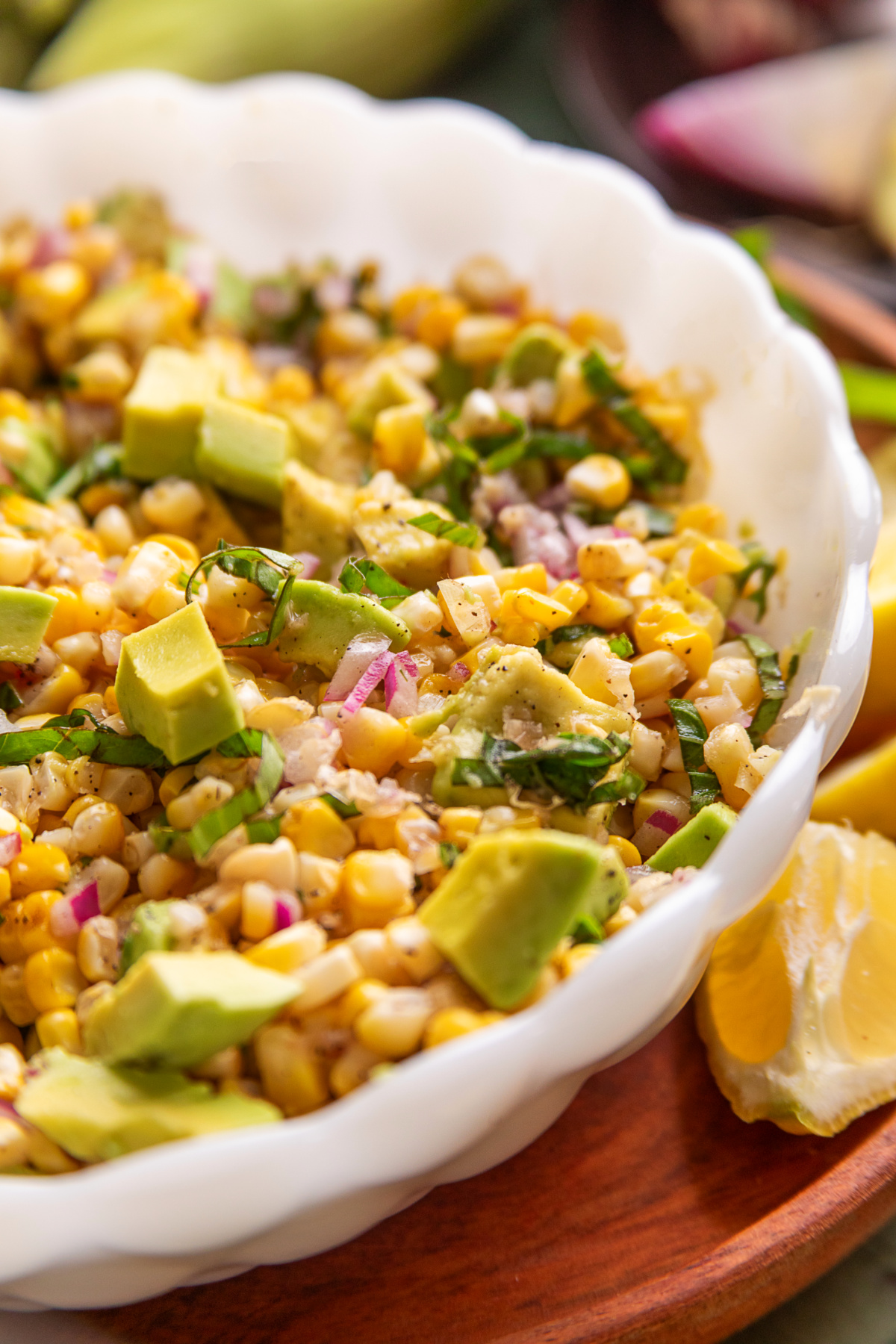 Close-up of grilled corn salad with avocado and basil in a serving bowl.