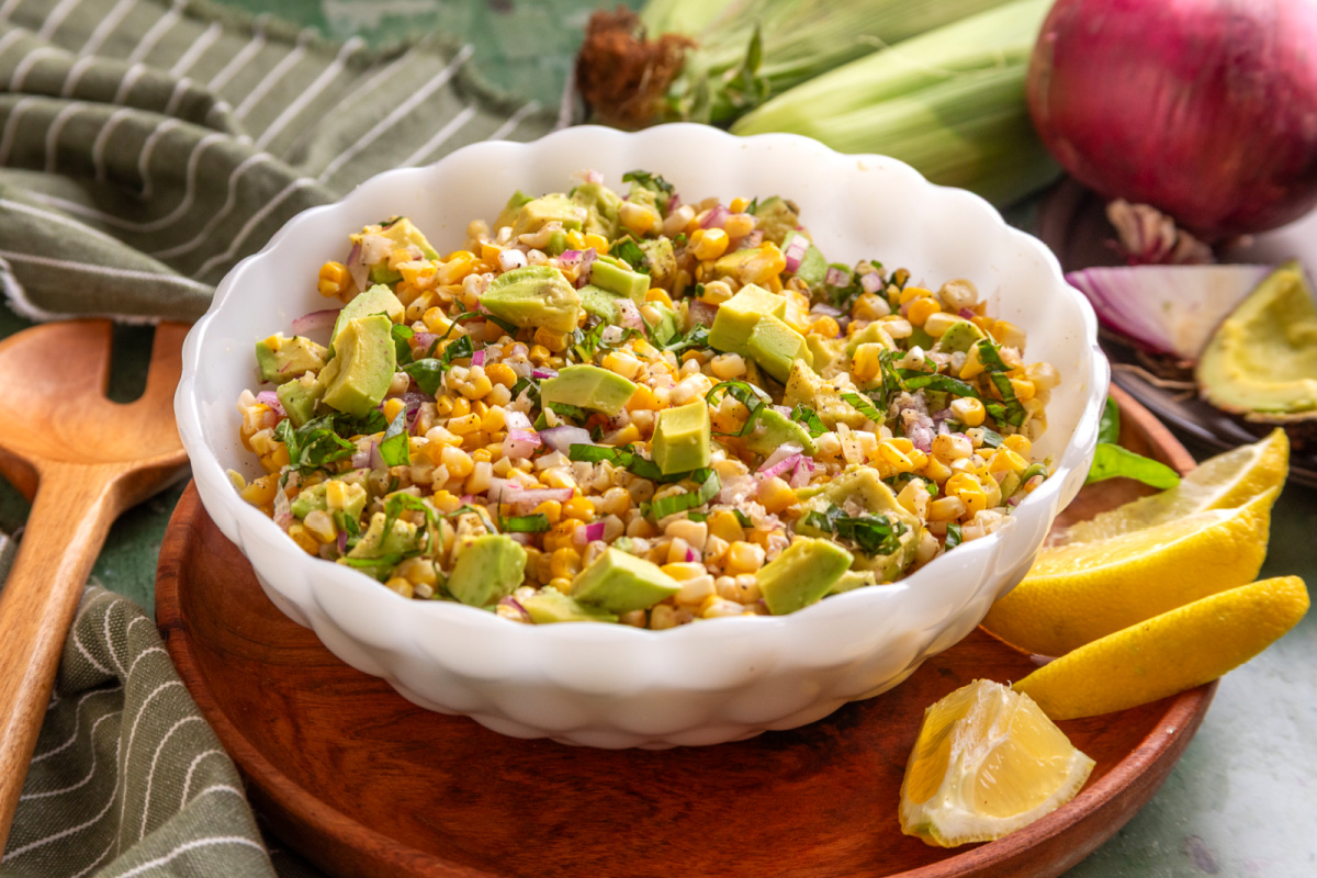 Serving bowl of grilled corn salad with avocado and basil tossed with red onion and a lemon vinaigrette.