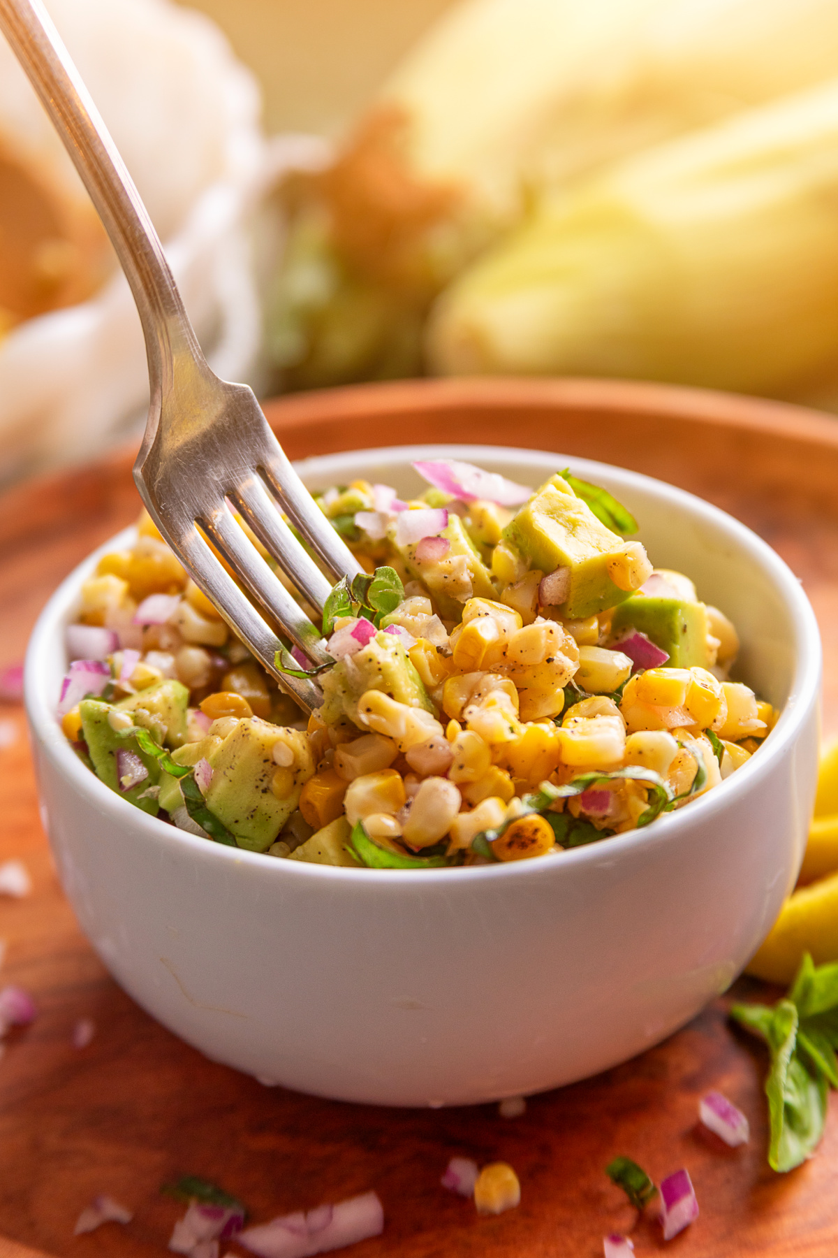 Fork lifting a bite of grilled corn salad with avocado, basil, and red onion.
