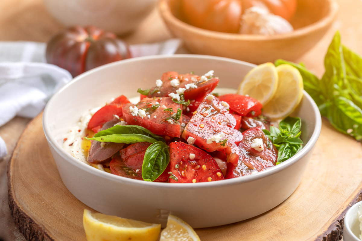 Serve heirloom tomato salad over whipped ricotta feta with toasted sourdough, crostini, or grilled baguette for scooping. heirloom-tomato-salad-over-whipped-ricotta-feta-serving-bowl