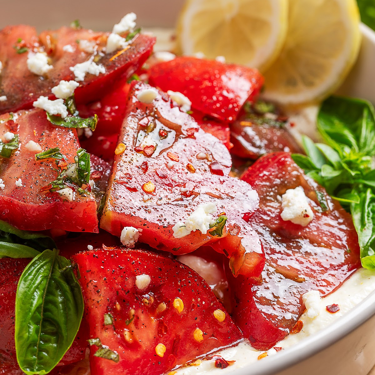 Close-up of heirloom tomato salad over whipped ricotta feta topped with fresh basil and lemon vinaigrette.