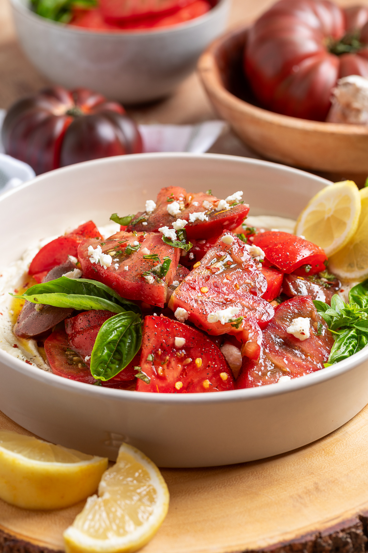Fresh heirloom tomatoes, creamy whipped ricotta-feta, basil, and a simple lemon vinaigrette come together in one easy summer salad. Vertical view of heirloom tomato salad with whipped ricotta feta, fresh basil, and lemon vinaigrette.