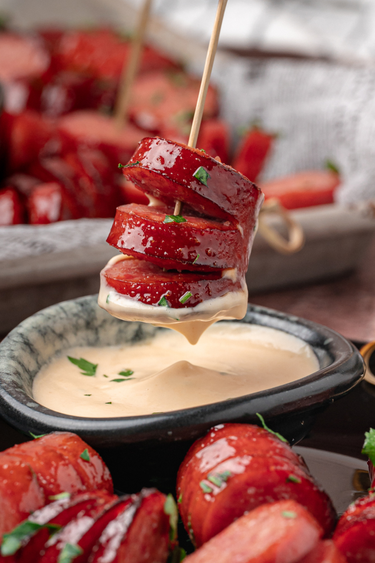 A glazed honey garlic kielbasa bite dipped into creamy honey mustard before serving. Close-up of a glazed honey garlic kielbasa bite on a skewer with creamy honey mustard.