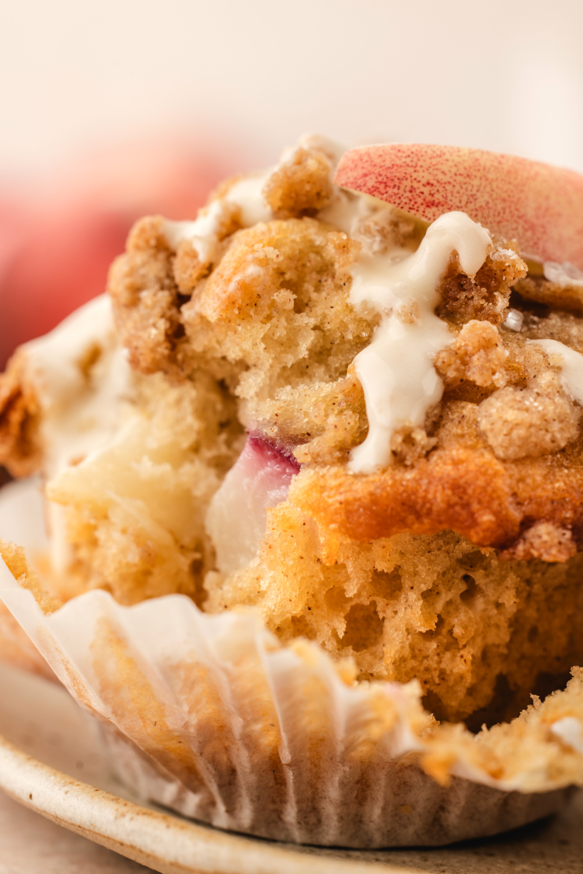 Close-up of the inside of a peach coffee cake muffin with fresh peach pieces, cinnamon streusel, and vanilla glaze