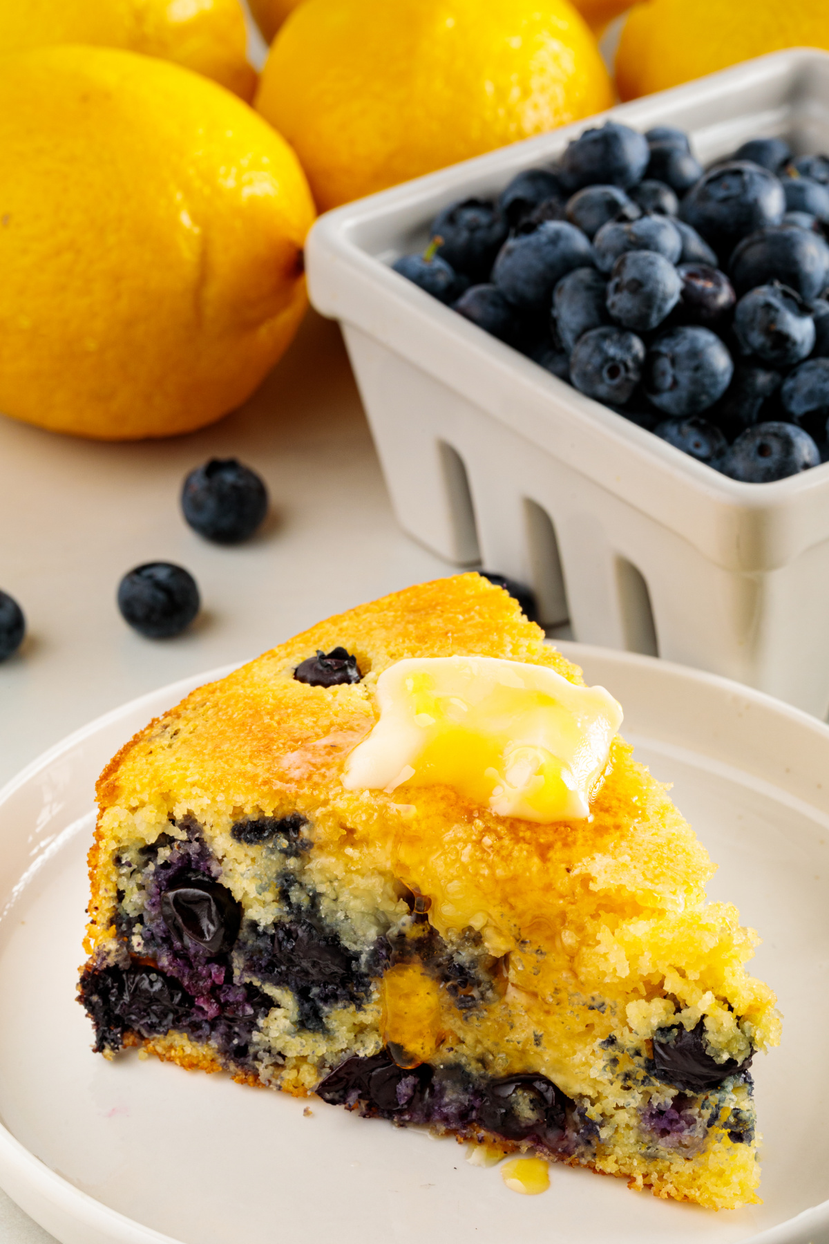 A warm slice of lemon blueberry cornbread with melting butter and honey drizzled over the top. Lemon blueberry cornbread served warm with butter and honey, showing fresh blueberries throughout the tender crumb.