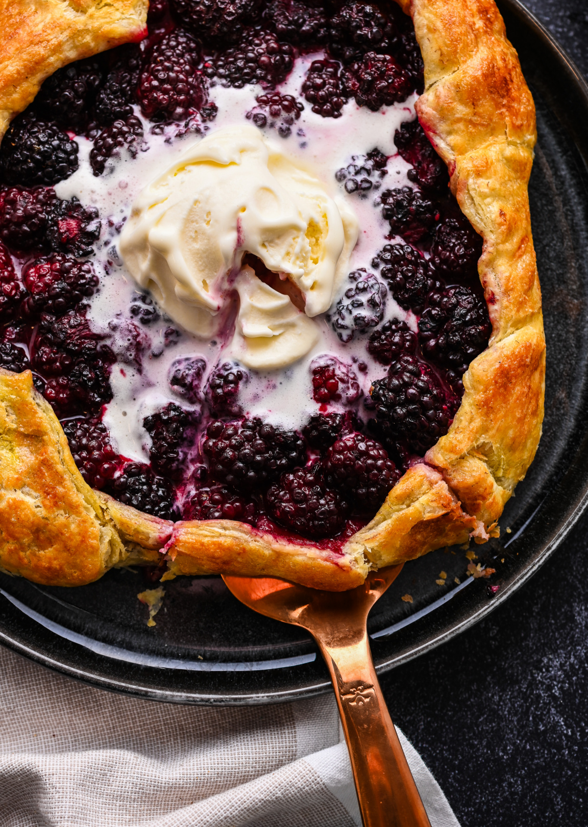 Lifting a slice of Blackberry Puff Pastry Galette with a pie server. Pie server lifting blackberry puff pastry galette topped with vanilla ice cream.