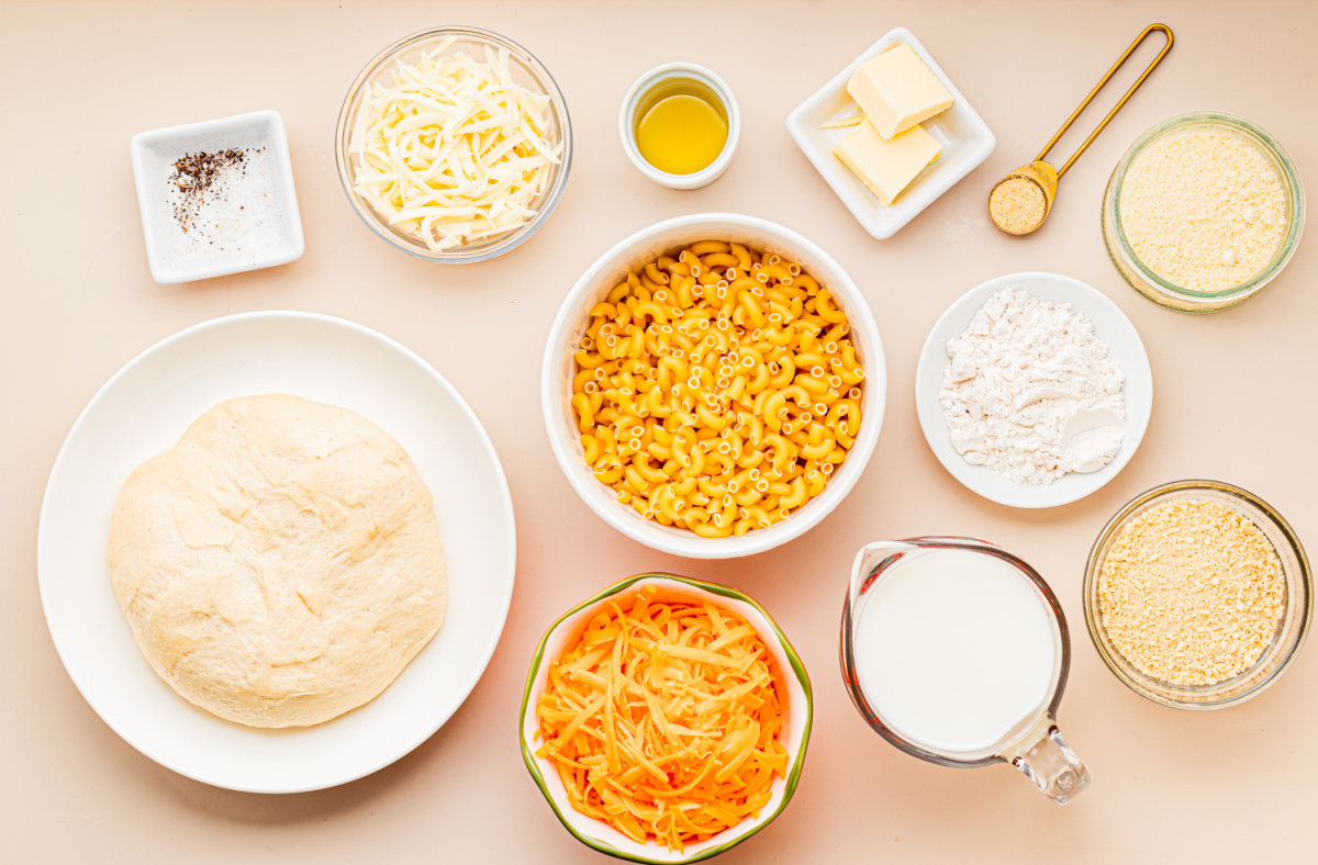 Ingredients for homemade mac and cheese pizza including pizza dough, elbow macaroni, cheddar, mozzarella, Parmesan, milk, butter, flour, olive oil, and panko breadcrumbs.