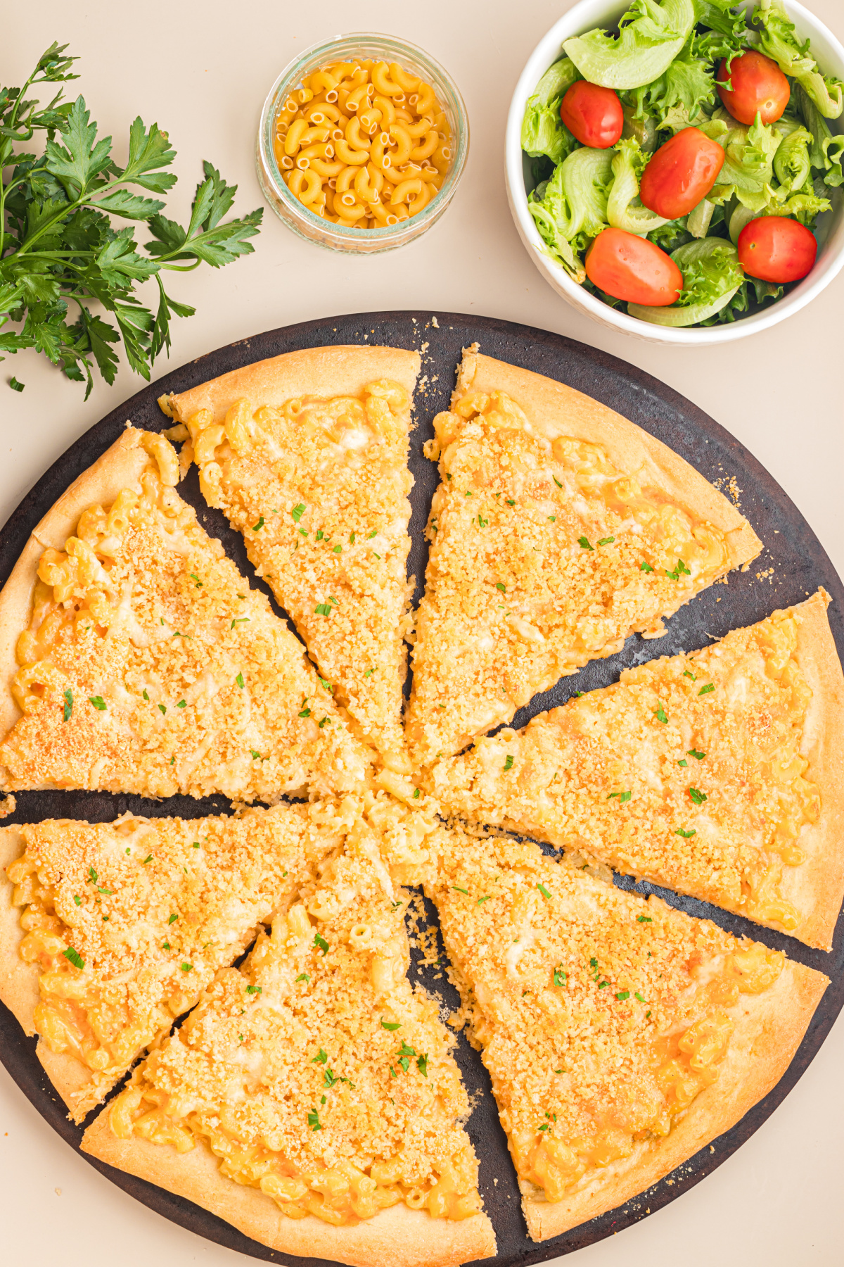 Kid-friendly mac and cheese pizza sliced into wedges with a buttery breadcrumb topping and served with a fresh green salad.