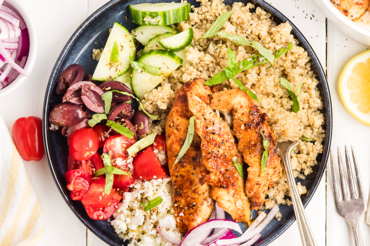 Overhead Mediterranean Chicken Bowl Overhead view of a Mediterranean chicken bowl with grilled chicken, quinoa, cherry tomatoes, cucumber, feta, Kalamata olives, red onion, basil, and lemon vinaigrette.