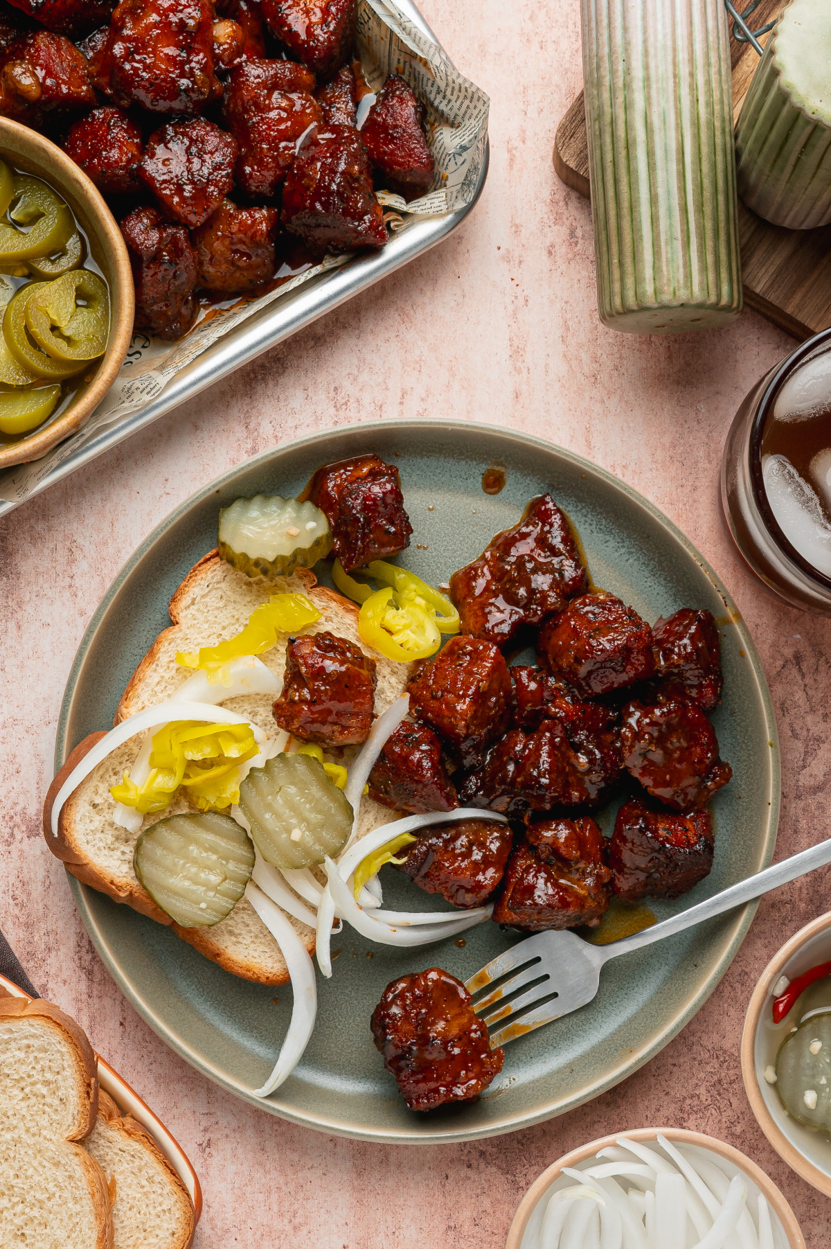 Oven pork belly burnt ends served with white bread, pickles, onions, and pepperoncini on a dinner plate.