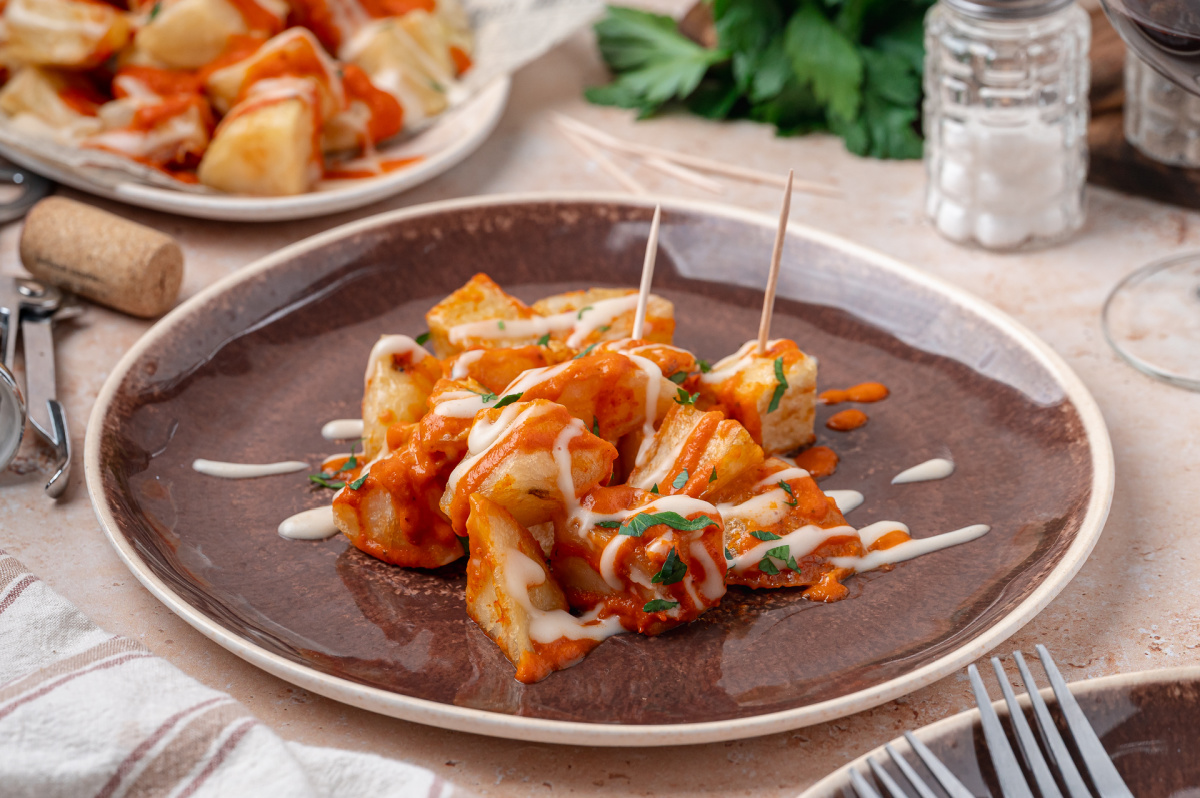 Patatas Bravas Appetizer Patatas bravas served on a plate with homemade bravas sauce, garlic aioli, and parsley.
