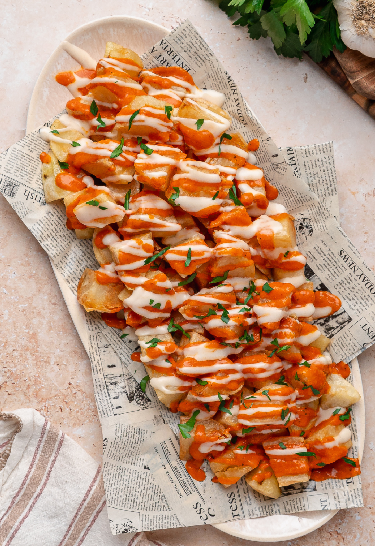 Patatas Bravas with Garlic Aioli Patatas bravas topped with homemade bravas sauce, garlic aioli, and fresh parsley on a serving platter.