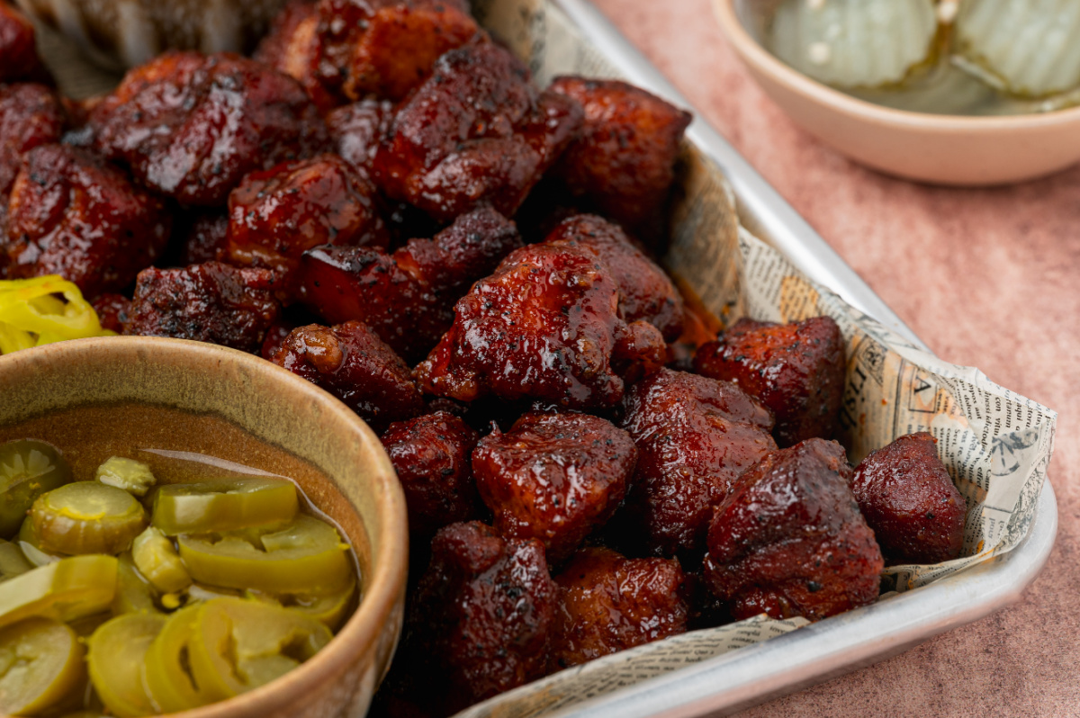 Close-up of Peach Tea Pork Belly Burnt Ends coated in a sticky caramelized peach tea glaze with sliced pickled jalape&ntilde;os.