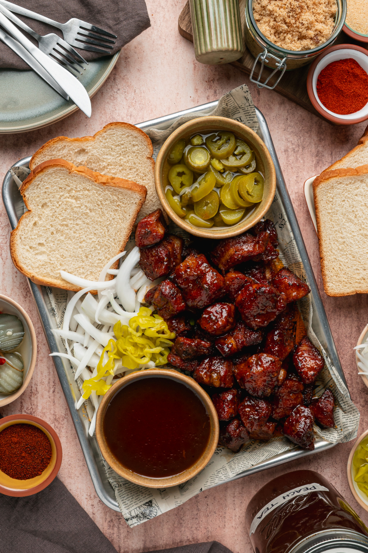 Peach Tea Pork Belly Burnt Ends served on a tray with sliced bread, pickled jalape&ntilde;os, onions, and extra peach tea glaze.