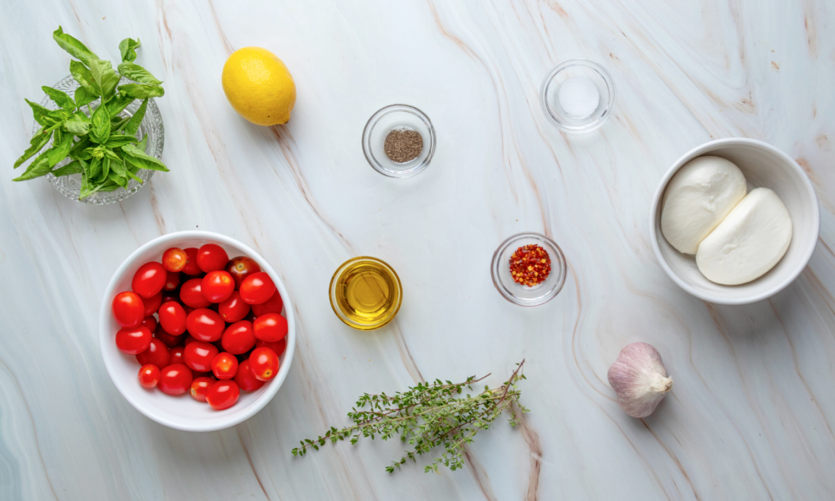 Ingredients needed to make Roasted Tomato Burrata Dip. Ingredients for Roasted Tomato Burrata Dip including burrata, grape tomatoes, olive oil, garlic, thyme, basil, lemon, sea salt, black pepper, and red pepper flakes.