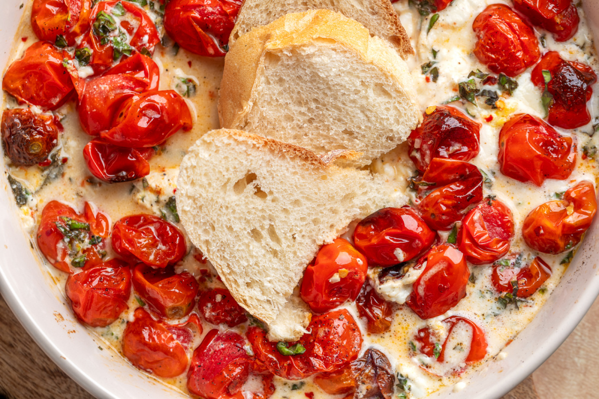Bread dipped into warm Roasted Tomato Burrata Dip. Bread dipped into Roasted Tomato Burrata Dip with roasted grape tomatoes, creamy burrata, basil, garlic, and lemon.