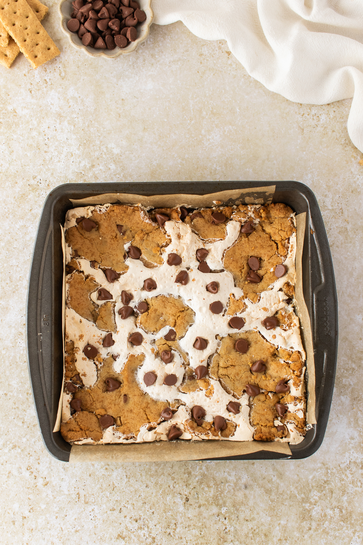 Freshly baked s'mores cookie bars in an 8x8-inch pan with toasted marshmallow and milk chocolate chips.