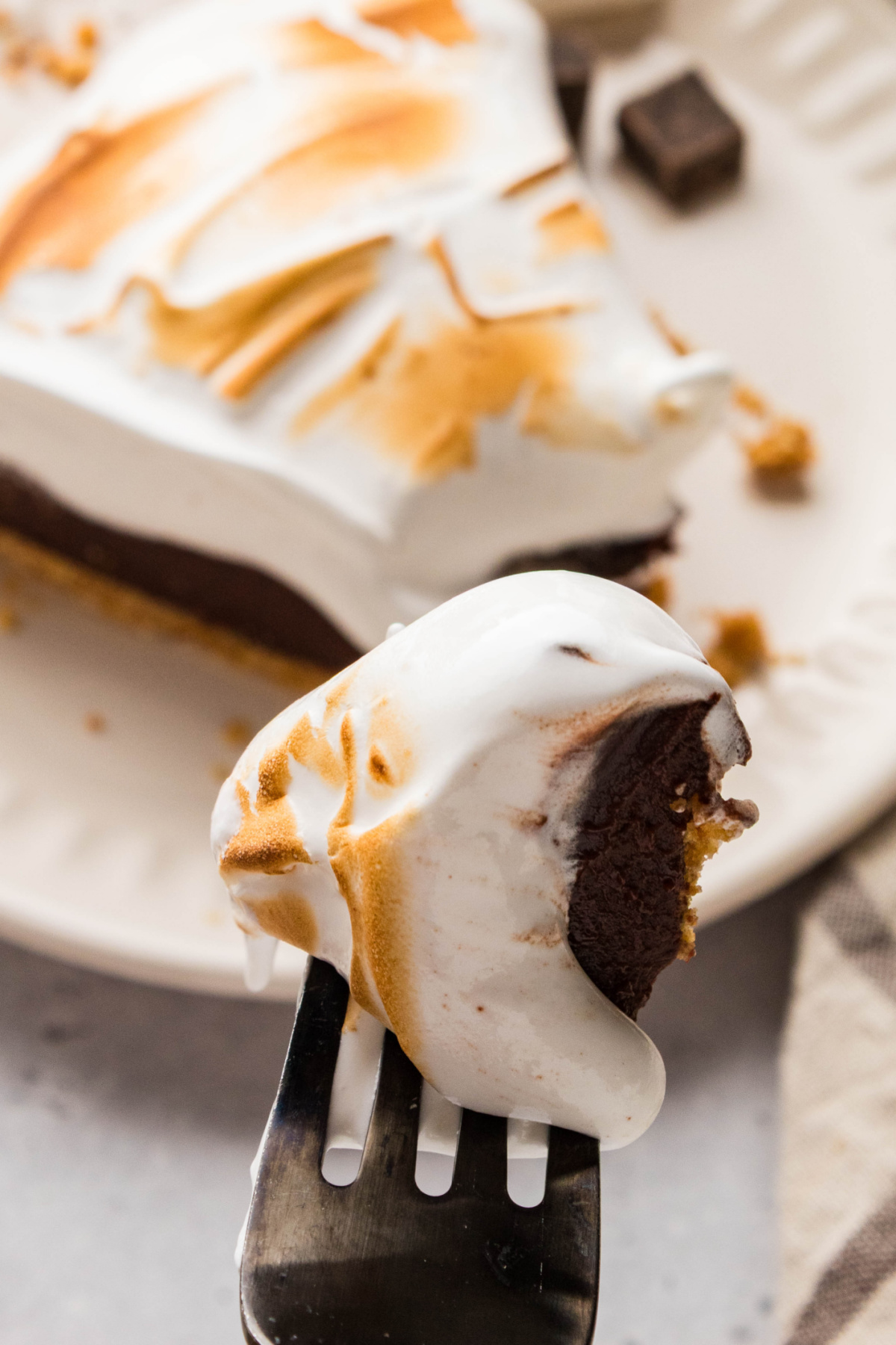 Fork holding a bite of s'mores pie with chocolate ganache, toasted homemade marshmallow topping, and graham cracker crust.
